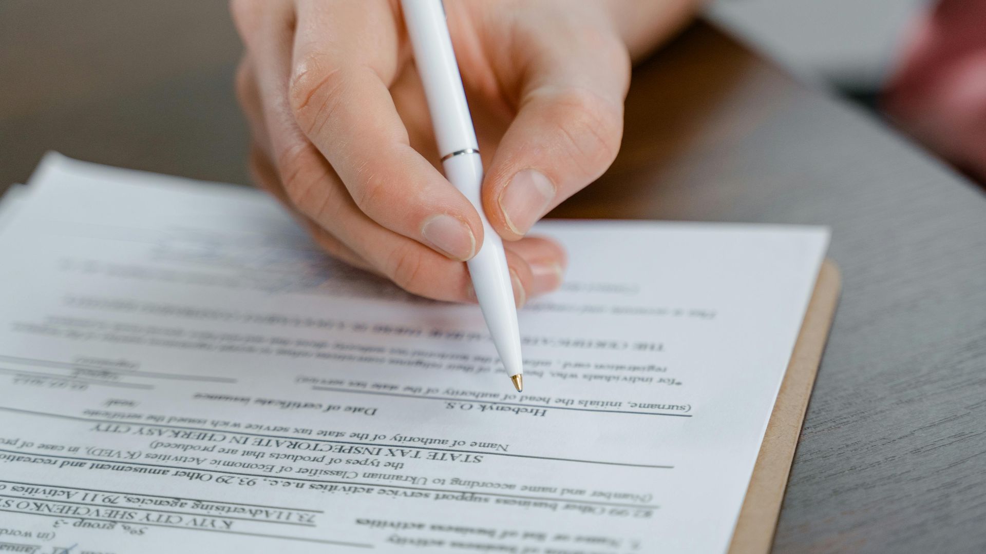A hand holding a pen signing a document, close-up shot with focus on the paper.