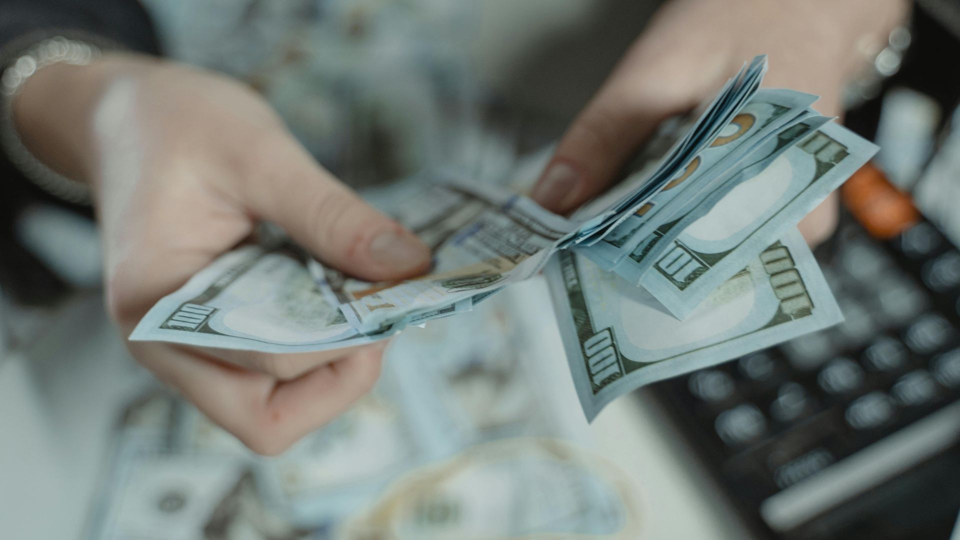 Close-up of hands counting hundred dollar bills with a calculator in the background.