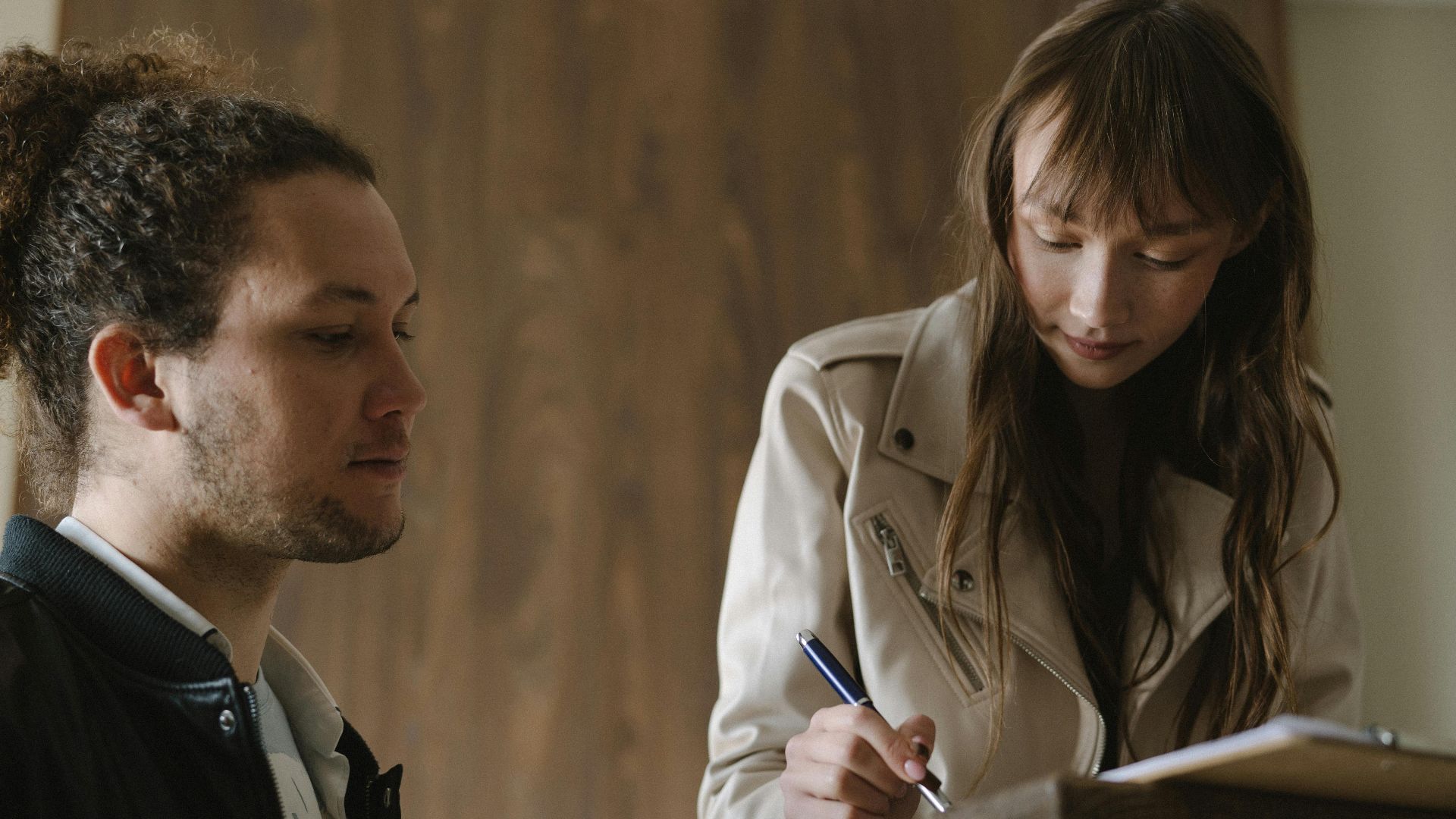 A young couple reviews and signs real estate documents indoors.