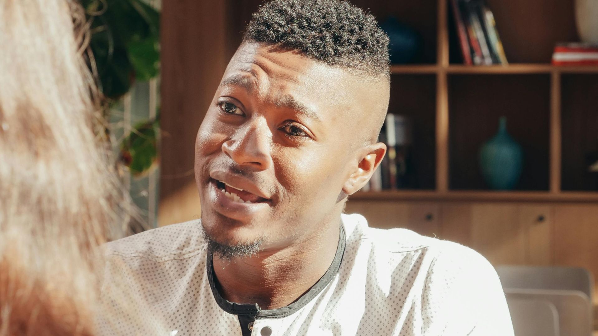 An African American man engaged in a conversation in a sunlit cafe.
