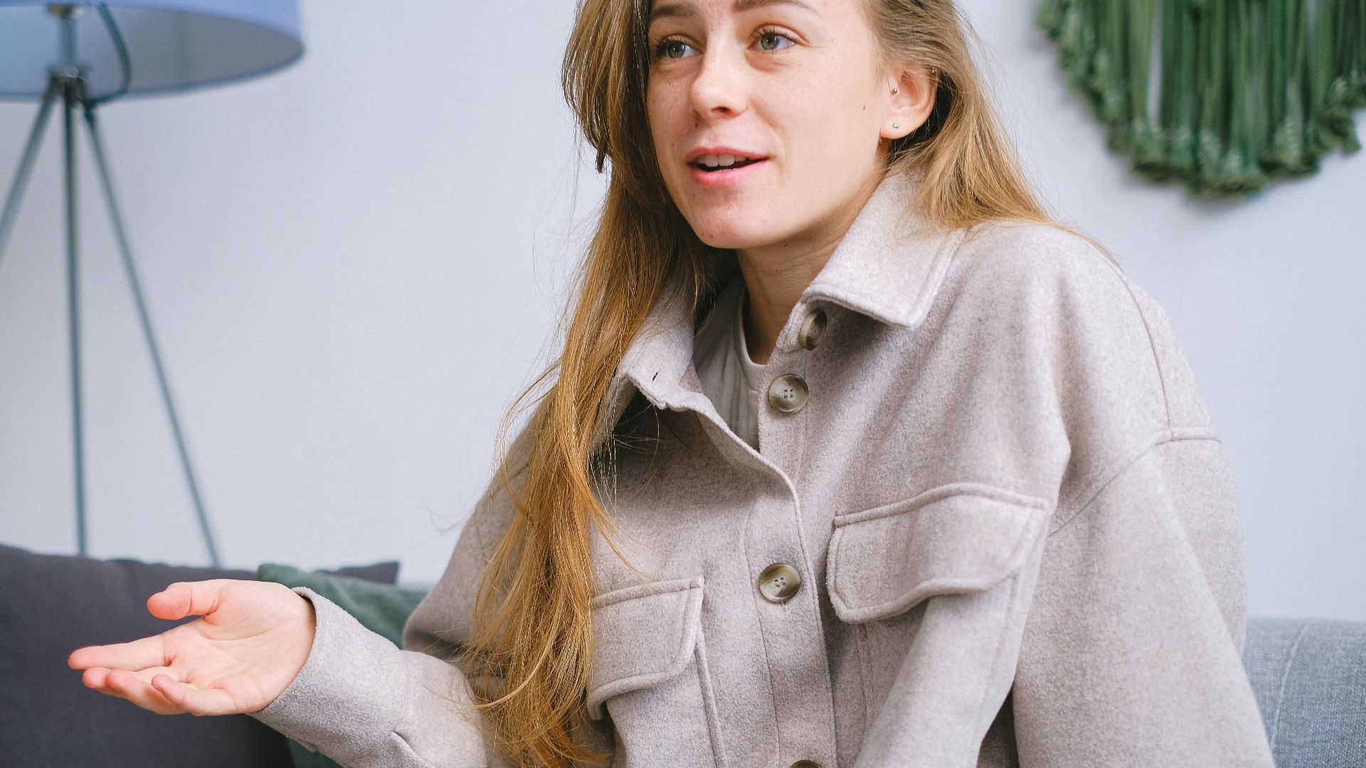Crop female with long hair in elegant clothes sitting on comfortable sofa while talking in light room during psychotherapy session