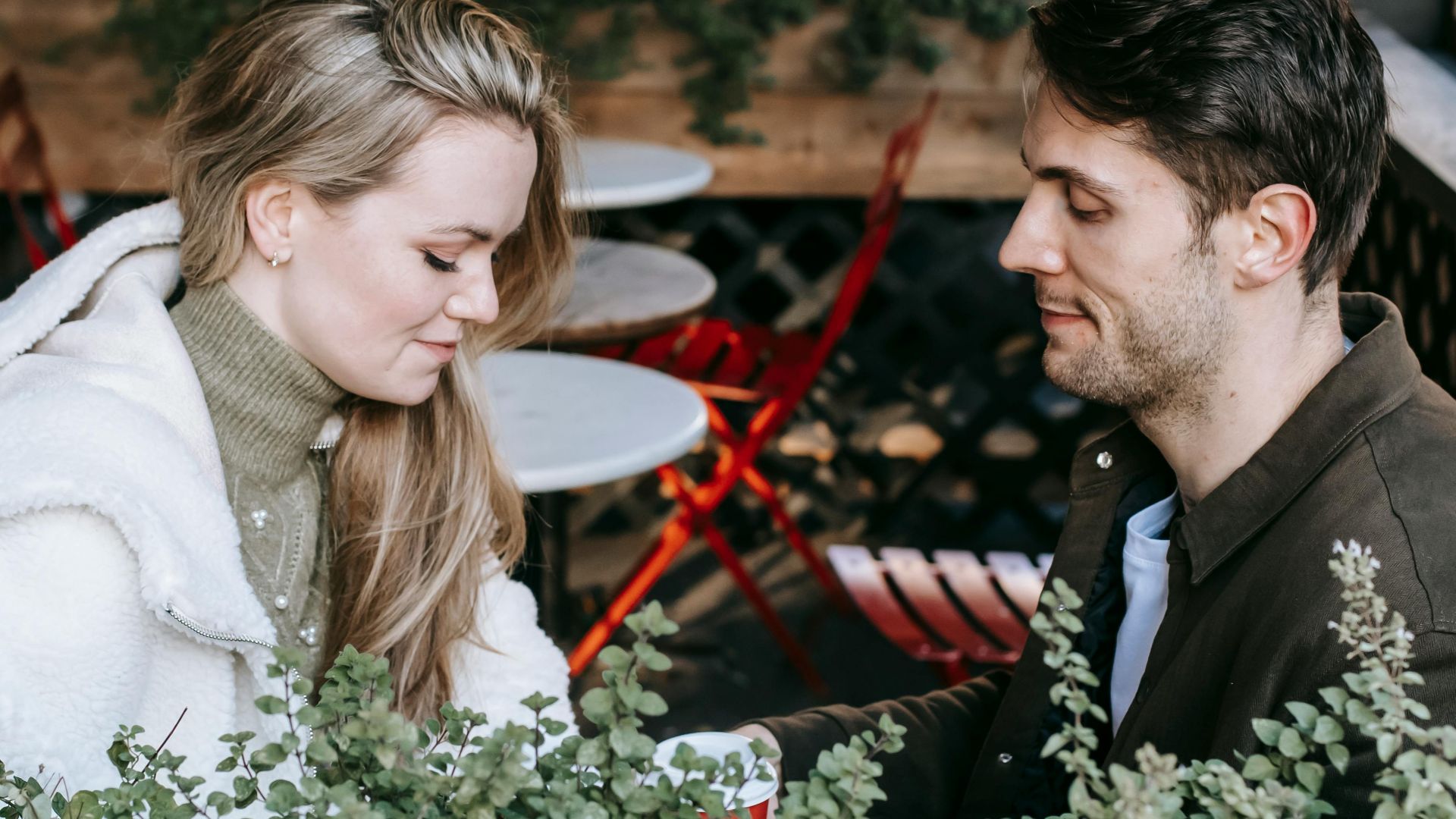 From above side view of calm young couple sitting on terrace decorated with potted plants and enjoying free time together