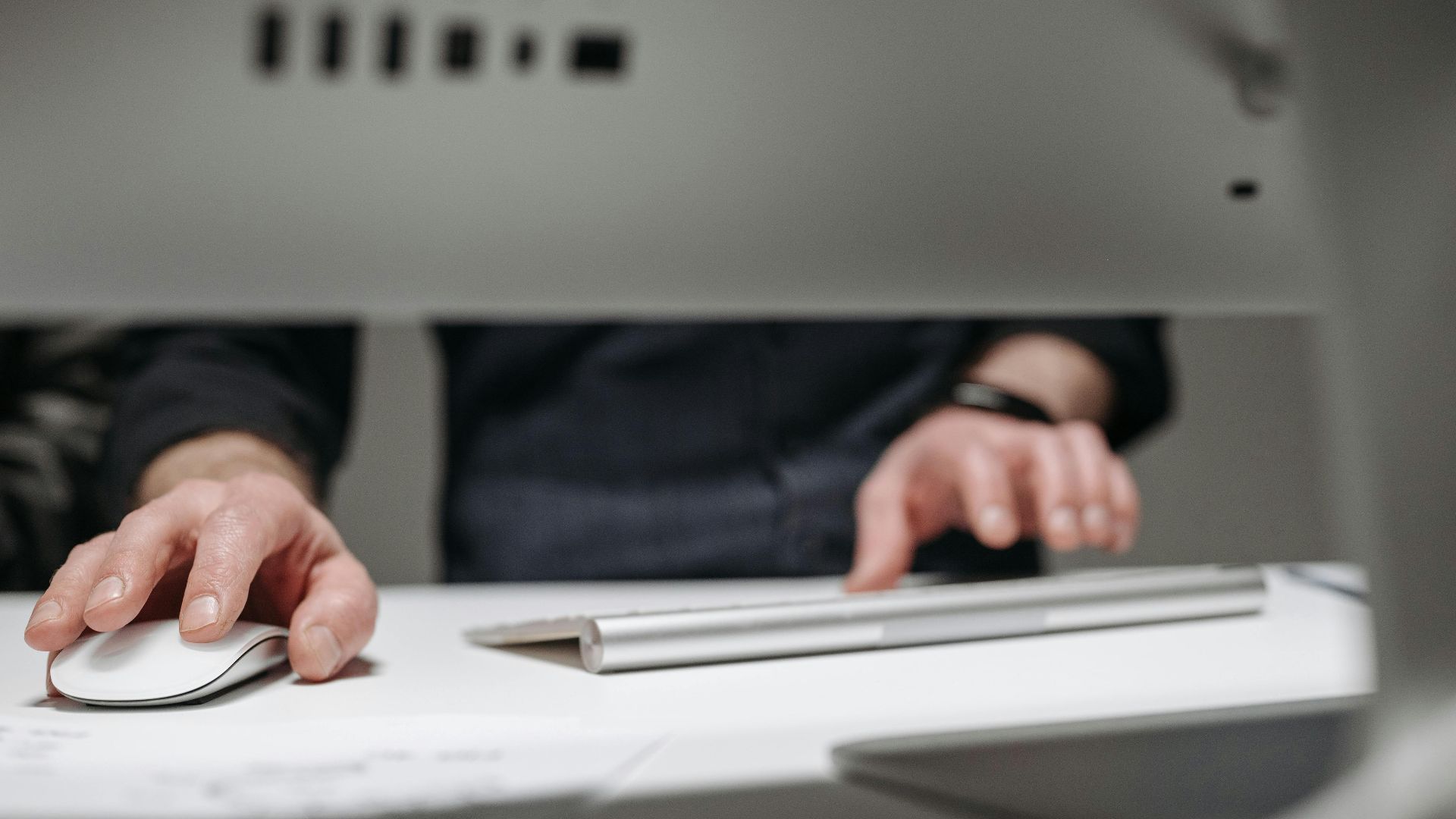 A focused close-up of hands typing on a sleek, modern computer setup in an office environment.