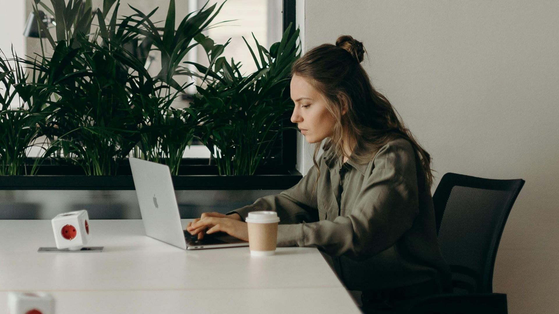 Woman working on a laptop in a minimalist home office with plants.