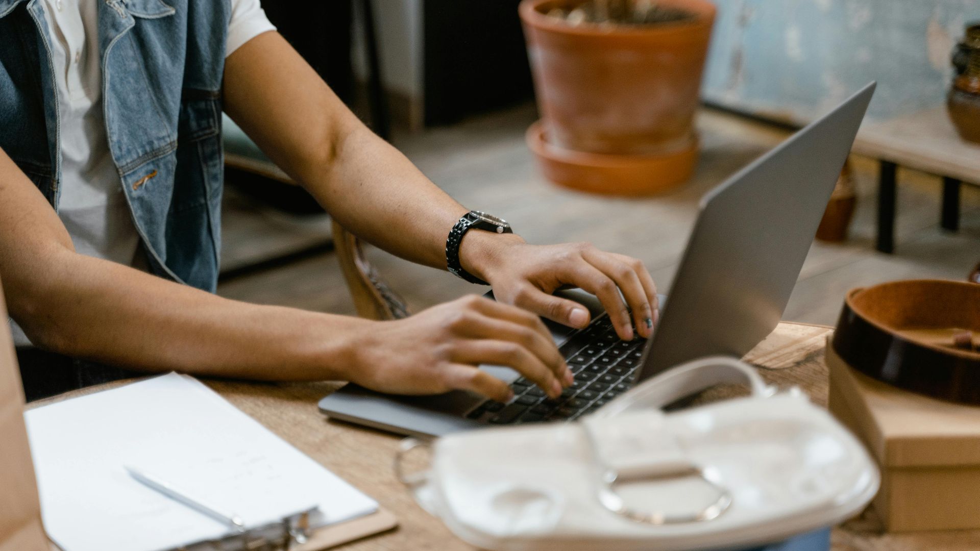 Close-up of hands typing on a laptop indoors with office accessories on a wooden table.