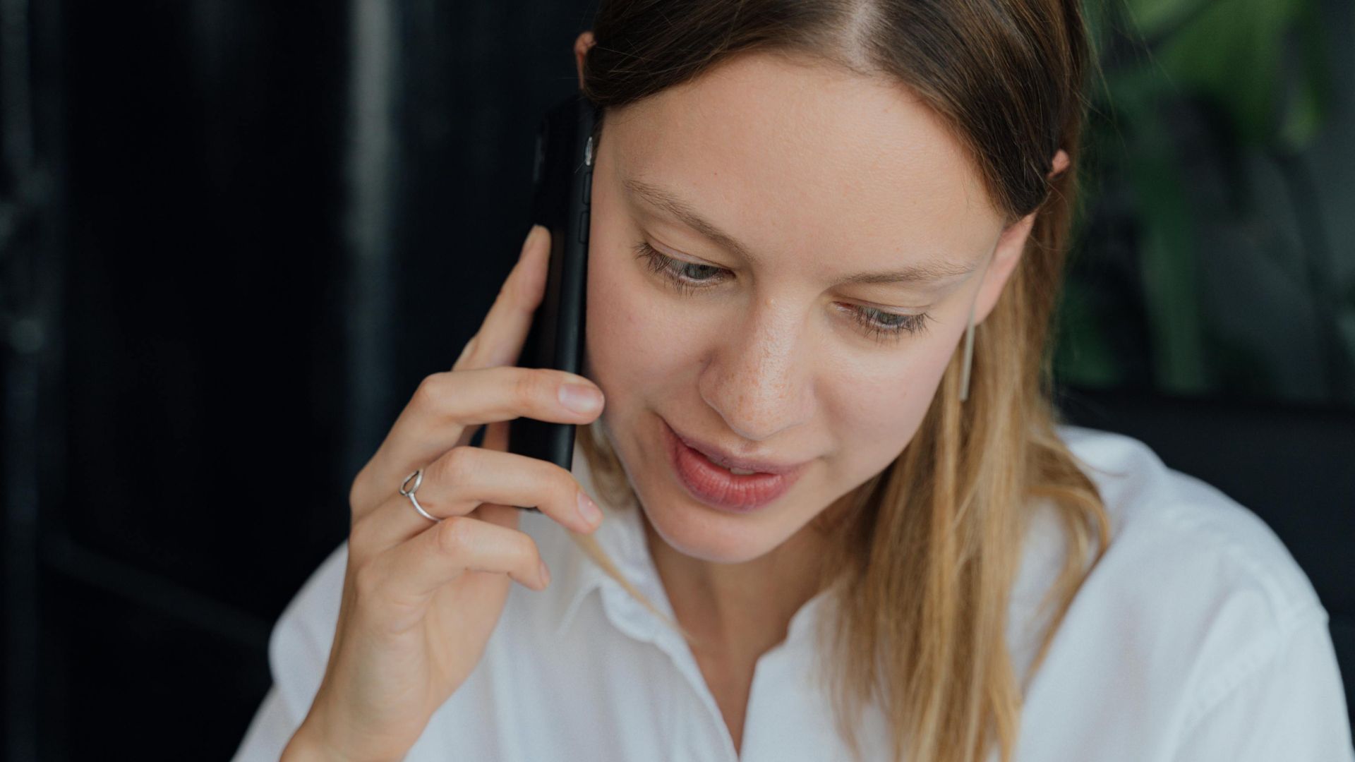 A professional woman in a white shirt making a phone call in an indoor setting, showing communication and business engagement.