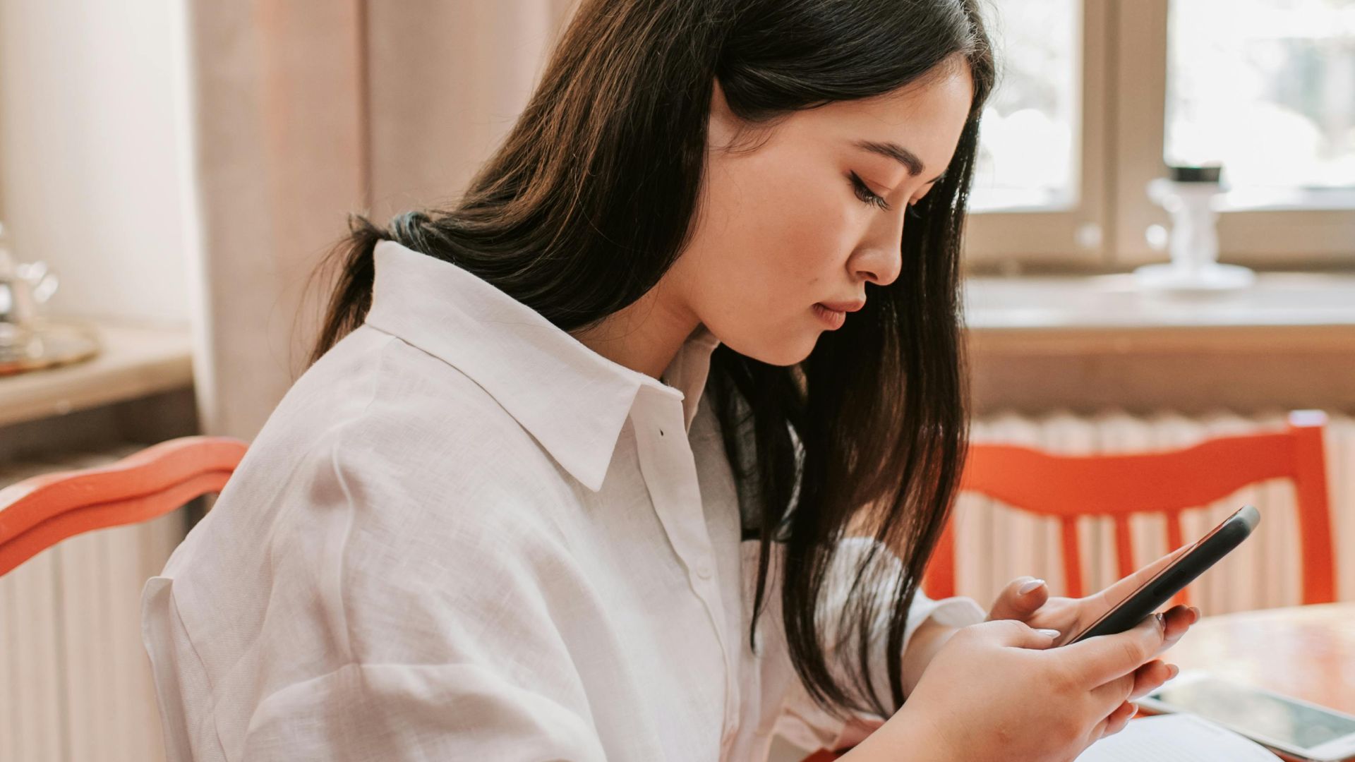 Focused young woman texting on smartphone at home office desk.