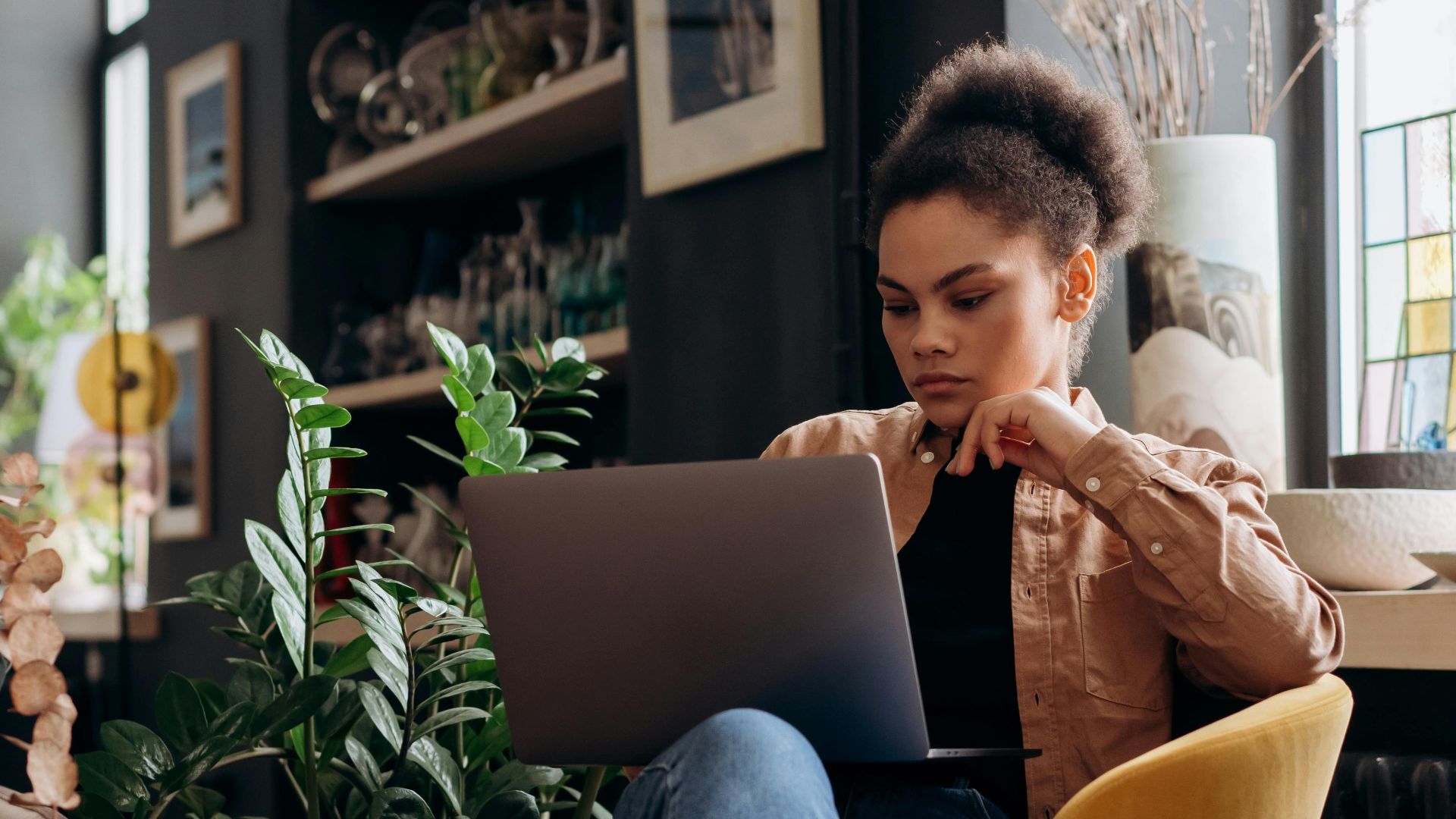 Focused woman working on laptop in a stylish home office environment, emphasizing a modern and relaxed work setting.