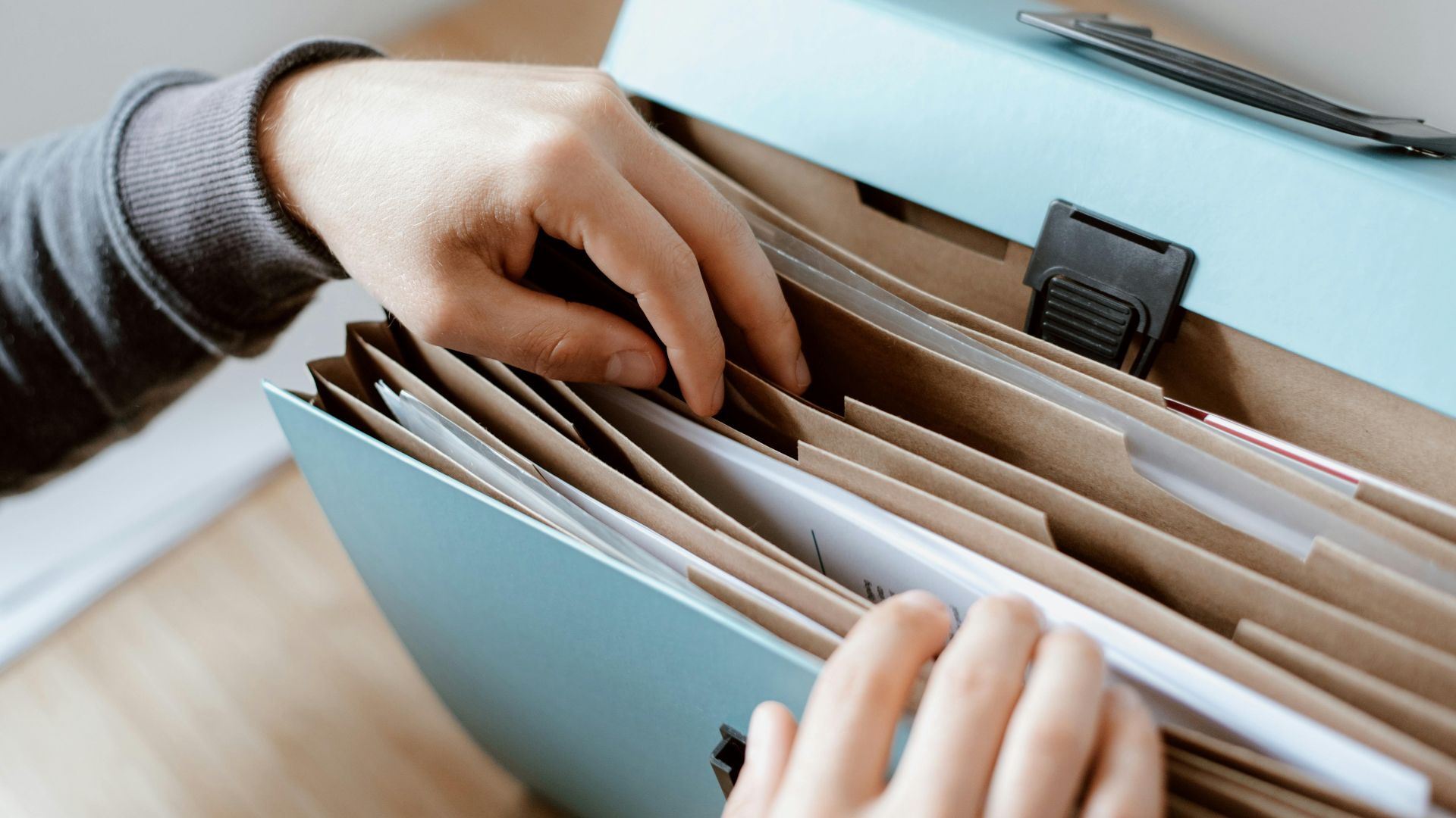 Crop unrecognizable person selecting document in opened briefcase for documents placed on wooden table