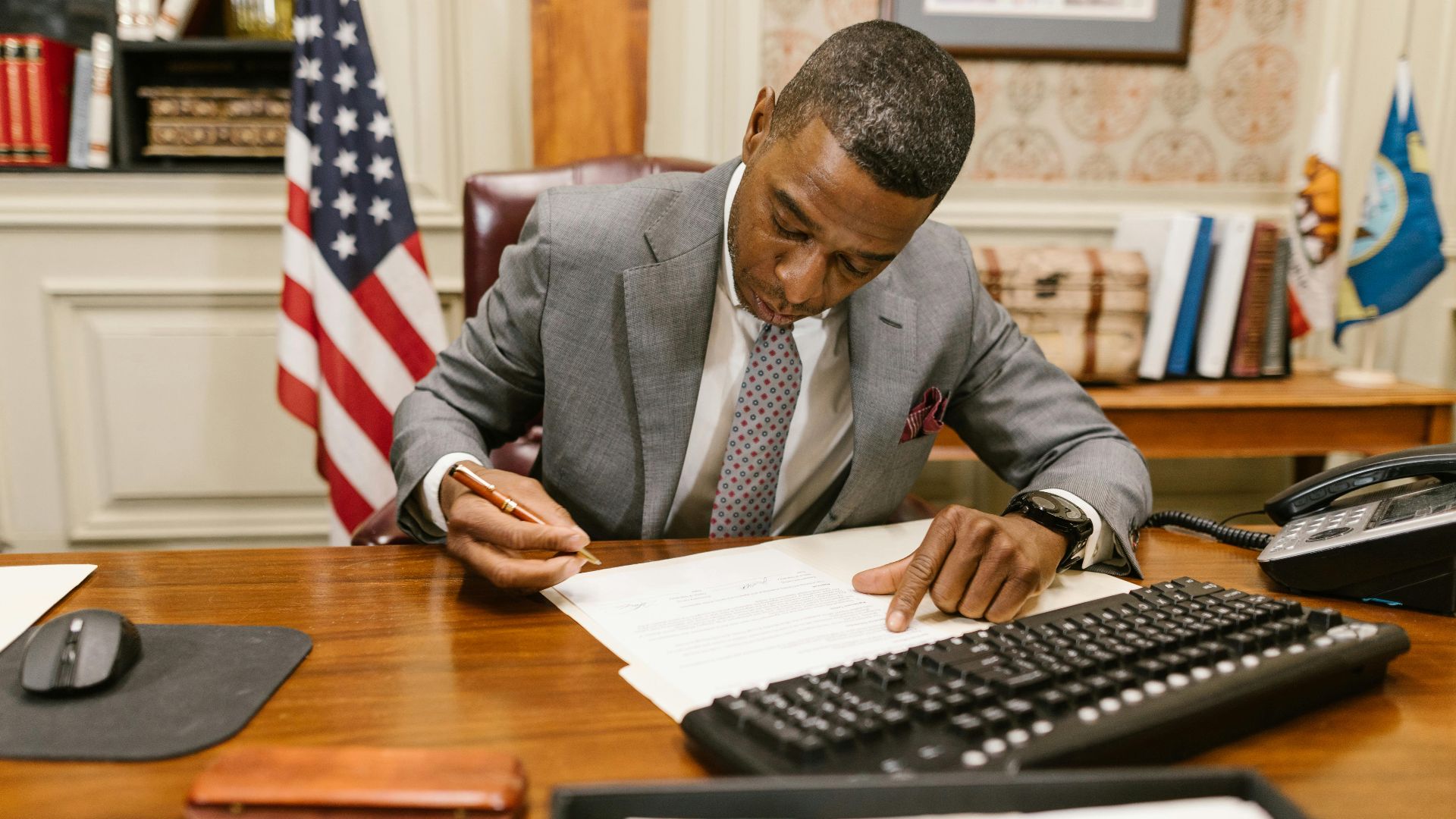 Professional man signs contract at desk in classic office environment.