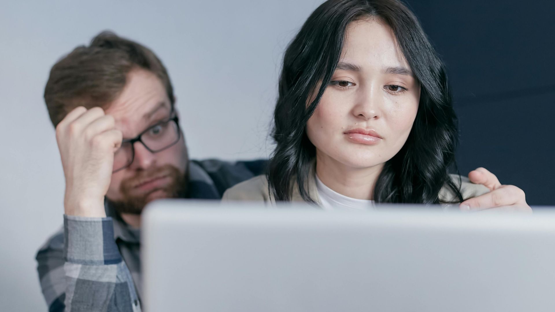 An interracial couple looking worried while checking finances at home.