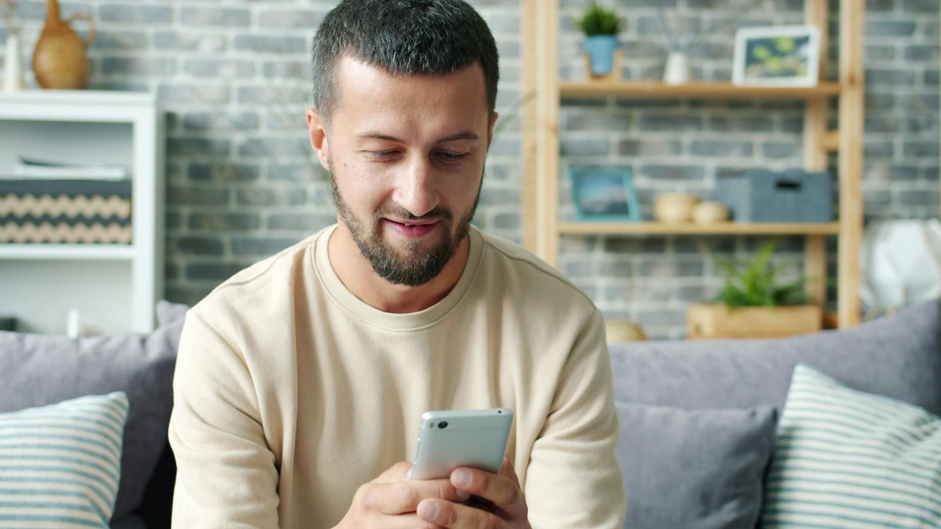 Casually dressed man using smartphone while sitting on a cozy sofa in a modern living room.