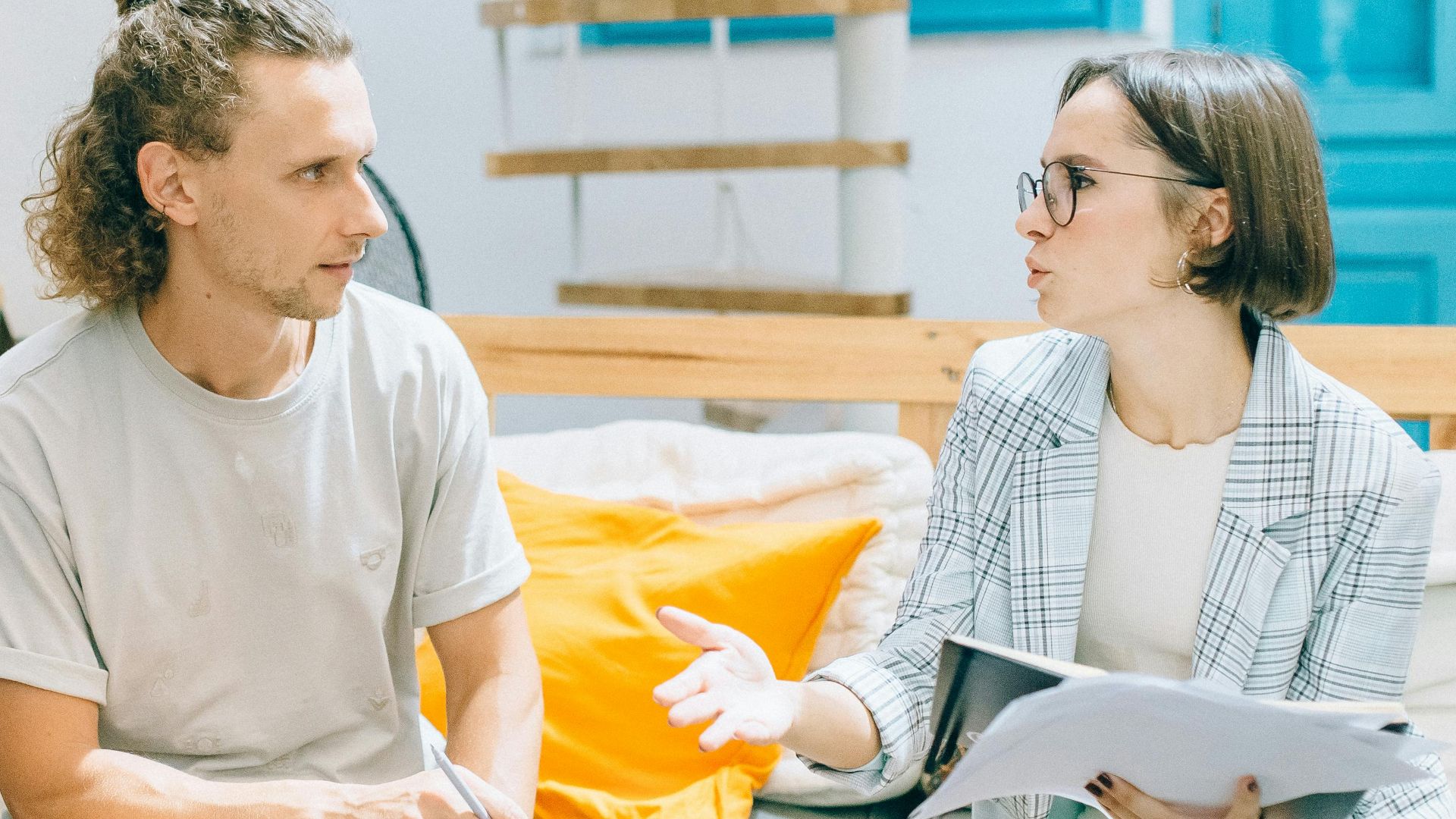 A man and woman discussing work in a stylish, bright living room setting.
