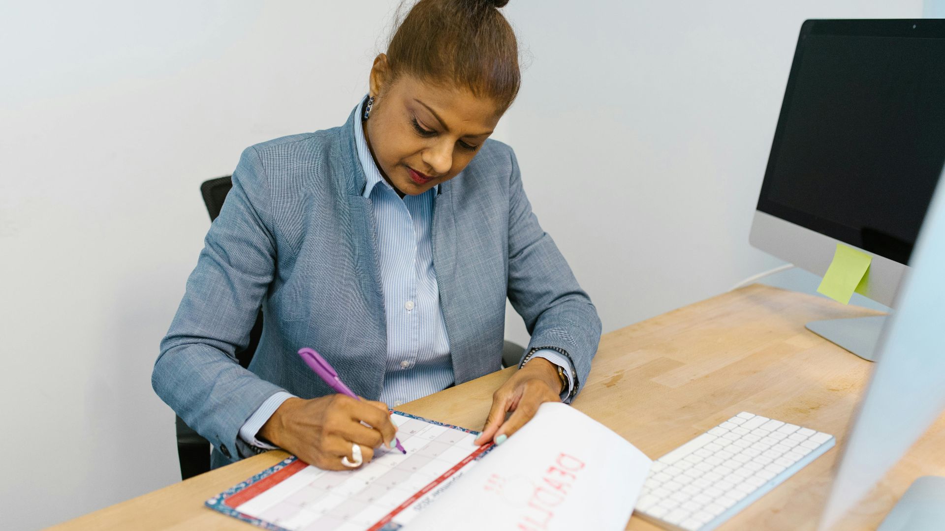 Businesswoman writing plans in a calendar at her office desk.