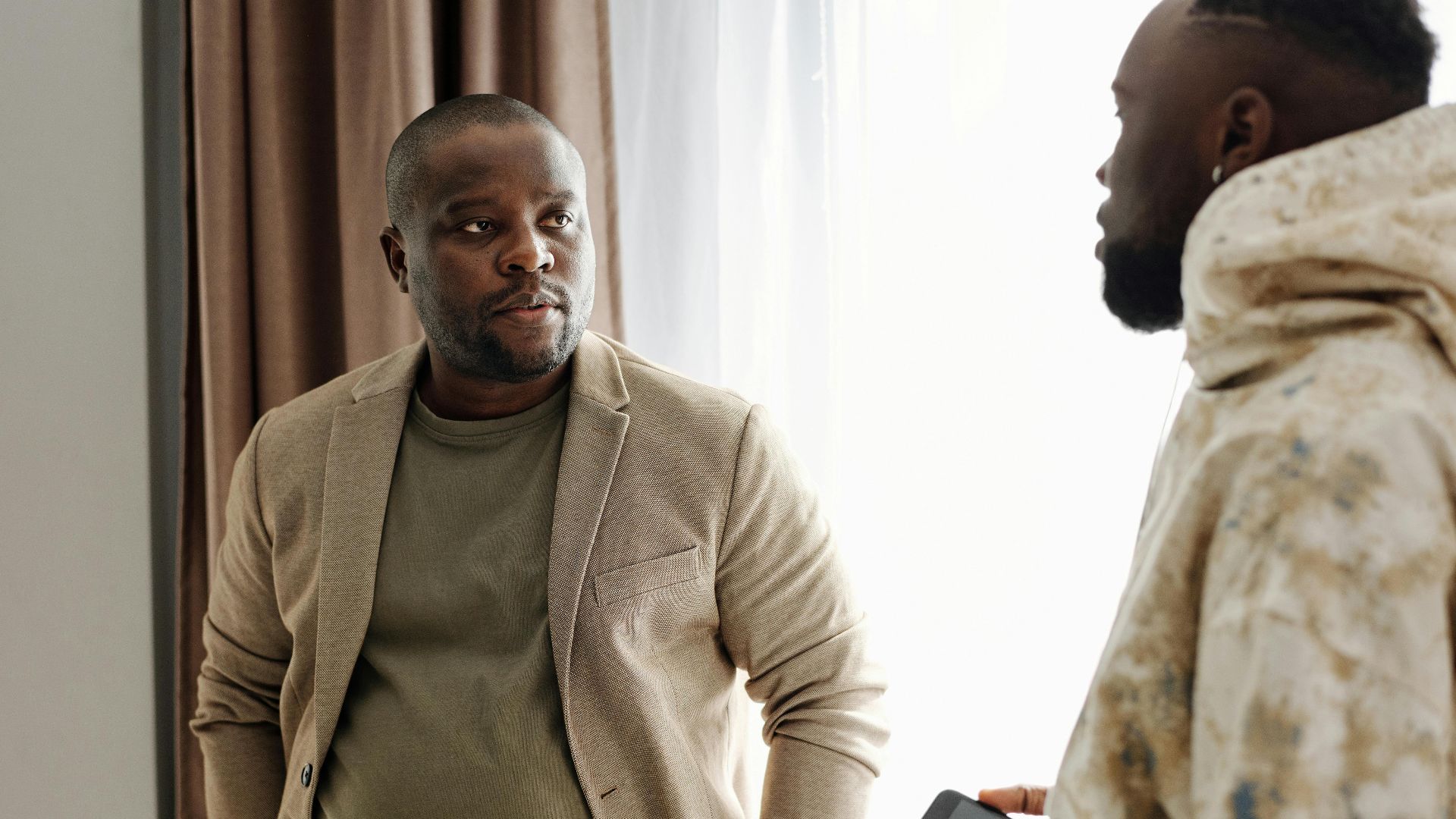 Two men engaged in a serious conversation indoors, one holding a smartphone.