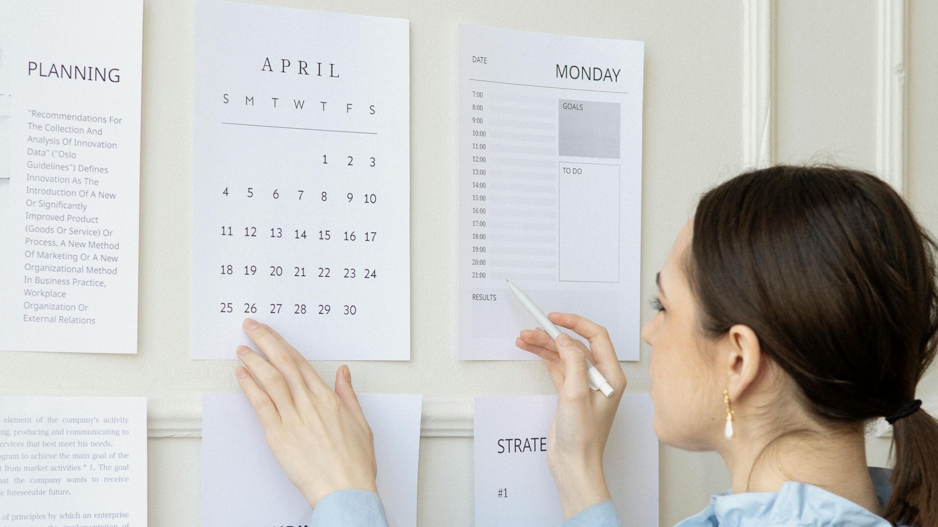 A woman arranging planning documents on an office wall, illustrating business strategy and organization.