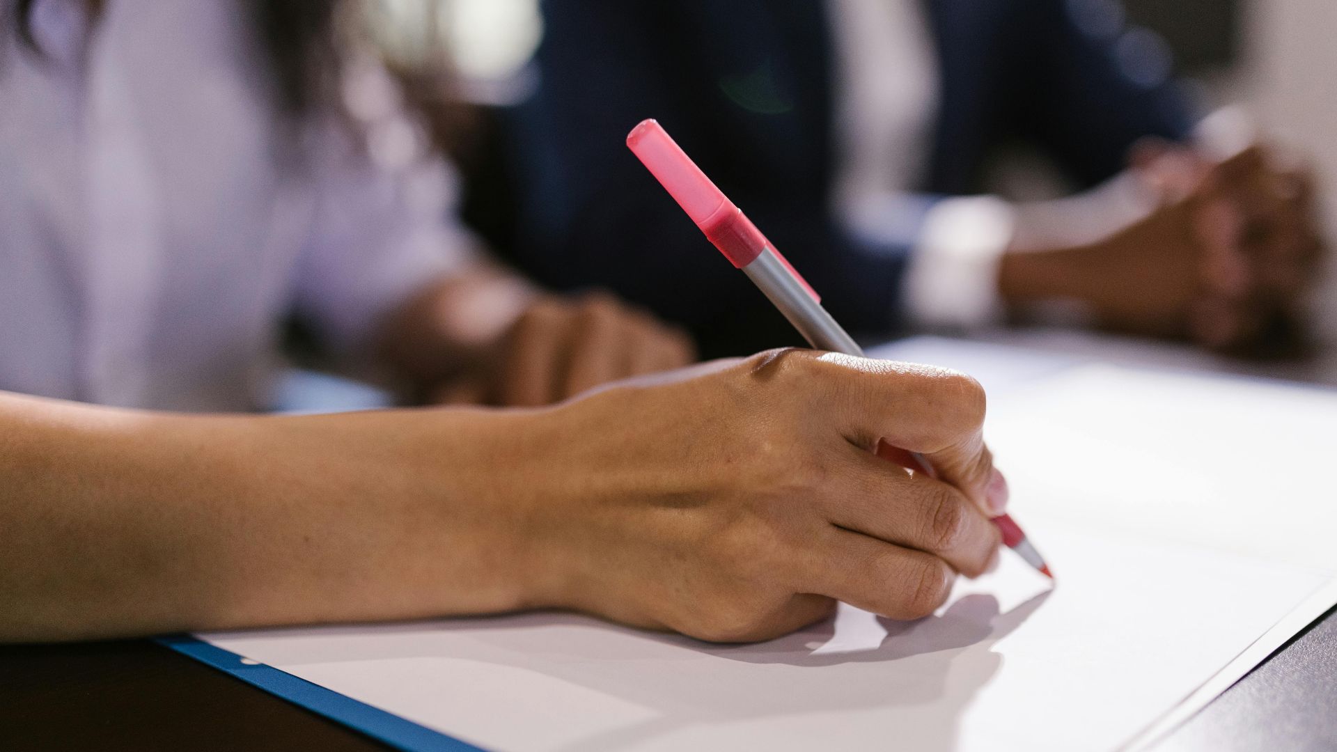 Detailed close-up of a person writing on paper with a pen in an office setting.