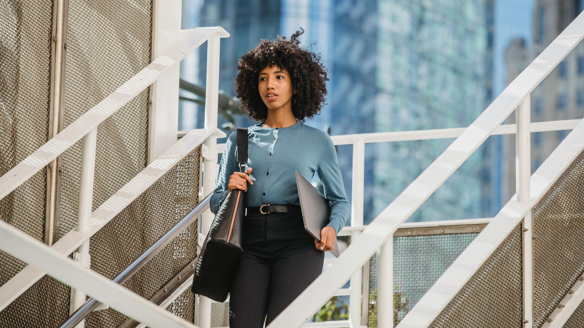 Confident woman carrying a laptop descends stairs in an urban business district.
