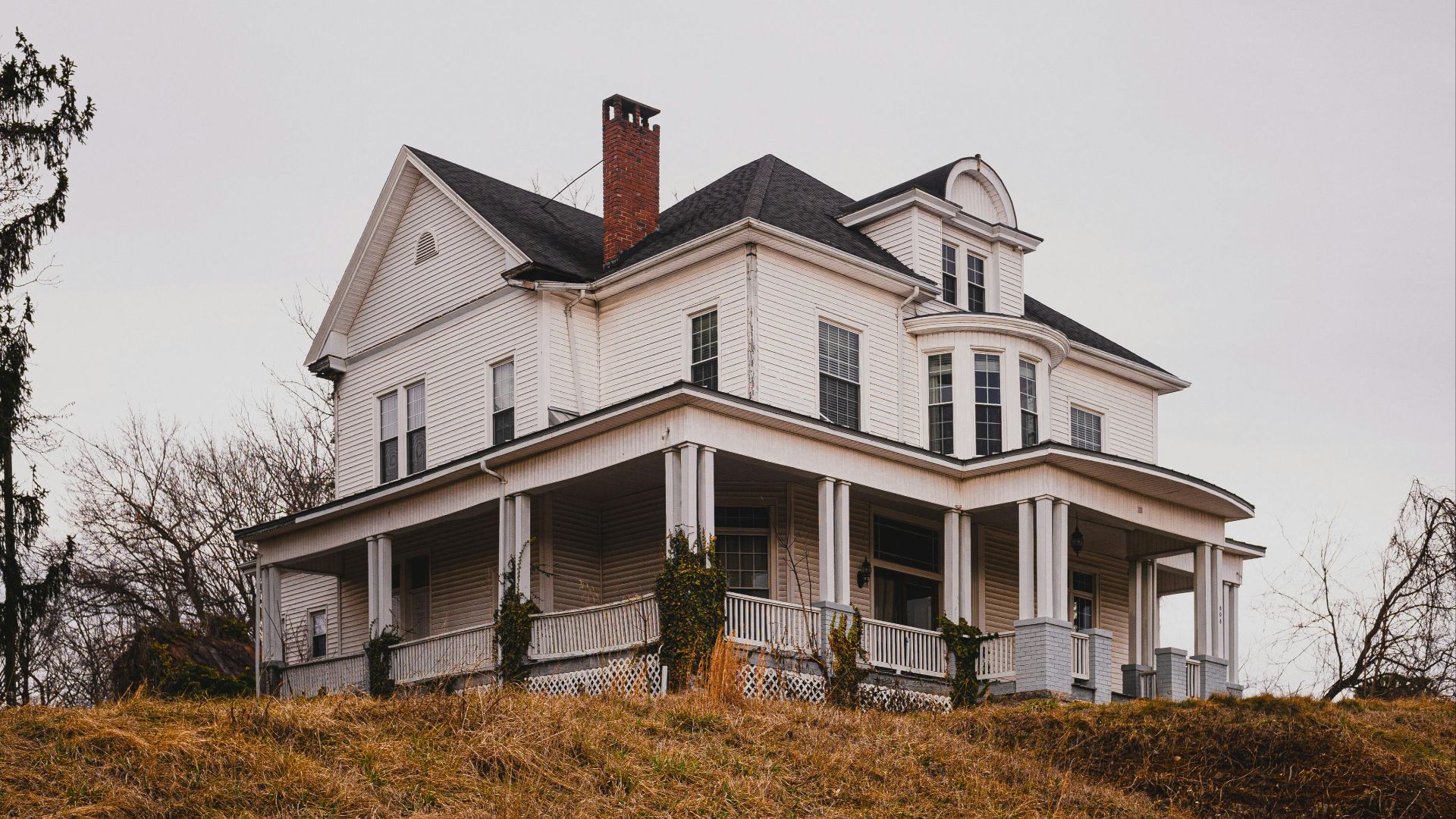 Beautiful historic white house with a wraparound porch set against autumn surroundings.