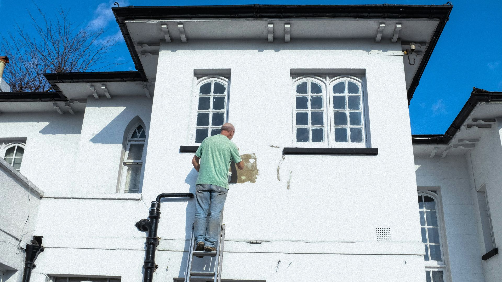 man in yellow shirt and blue denim jeans standing on white concrete building during daytime