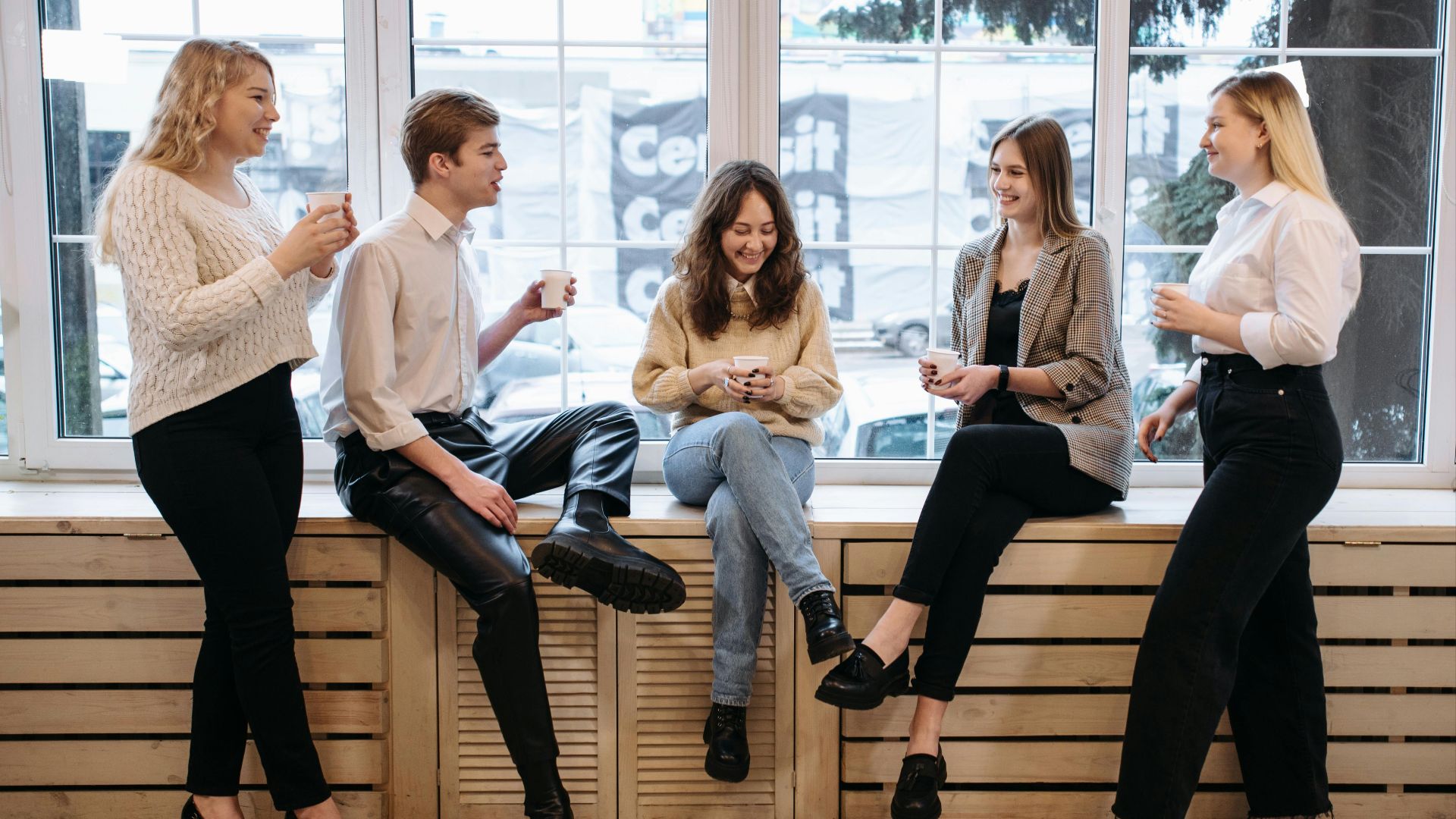 Group of coworkers enjoying a coffee break by the window in an office setting.