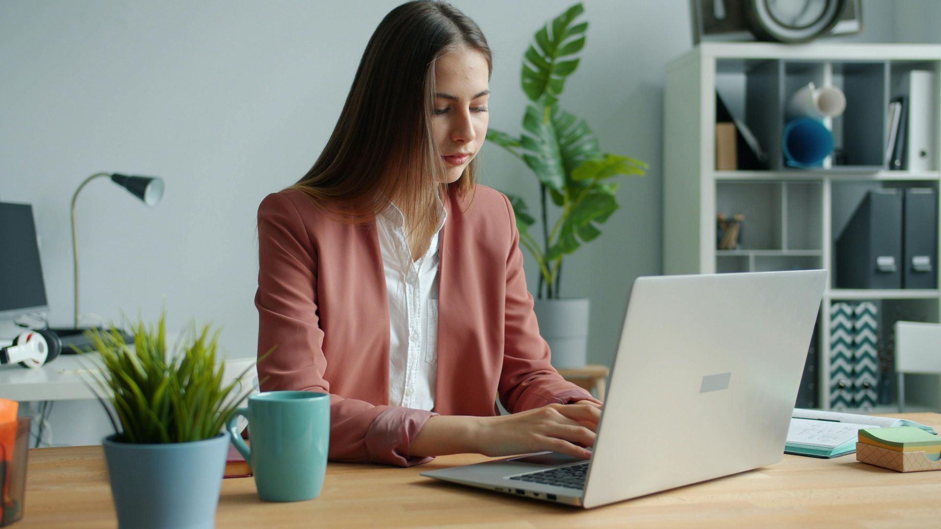 Confident young woman in business attire working on computer in modern office setting.