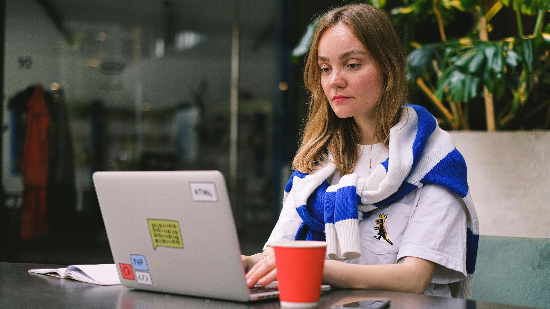Young woman focused on laptop work in a modern cafe setting, surrounded by technology.