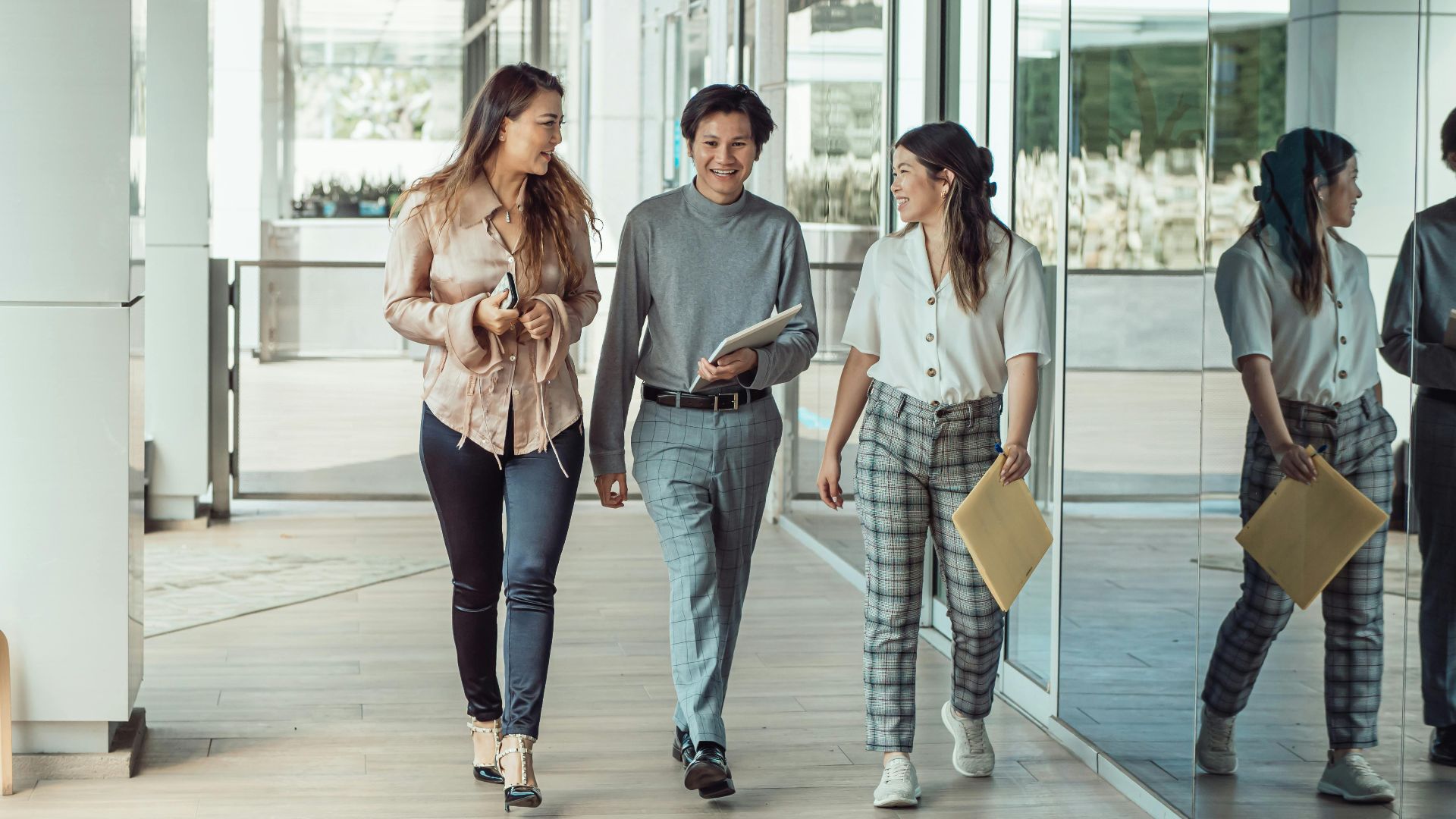 Three colleagues walking and conversing in a modern office, reflecting teamwork and collaboration.