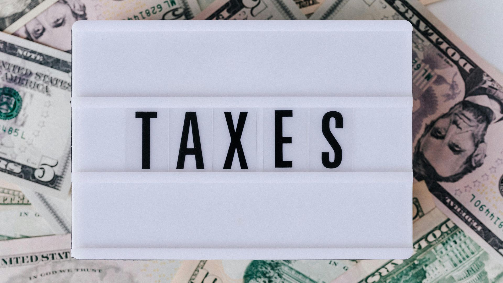 Top view of white vintage light box with TAXES inscription placed on stack of USA dollar bills on white surface