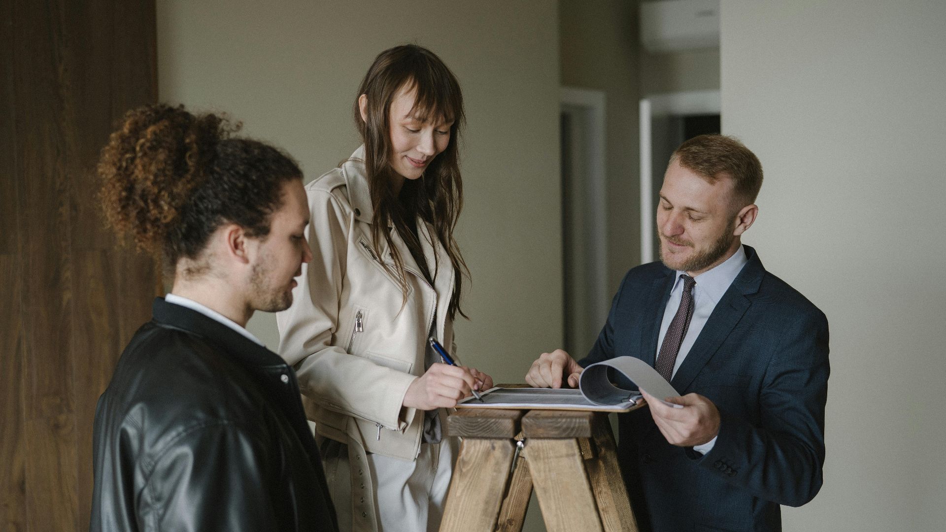 A couple signing real estate documents with a realtor inside a new apartment.