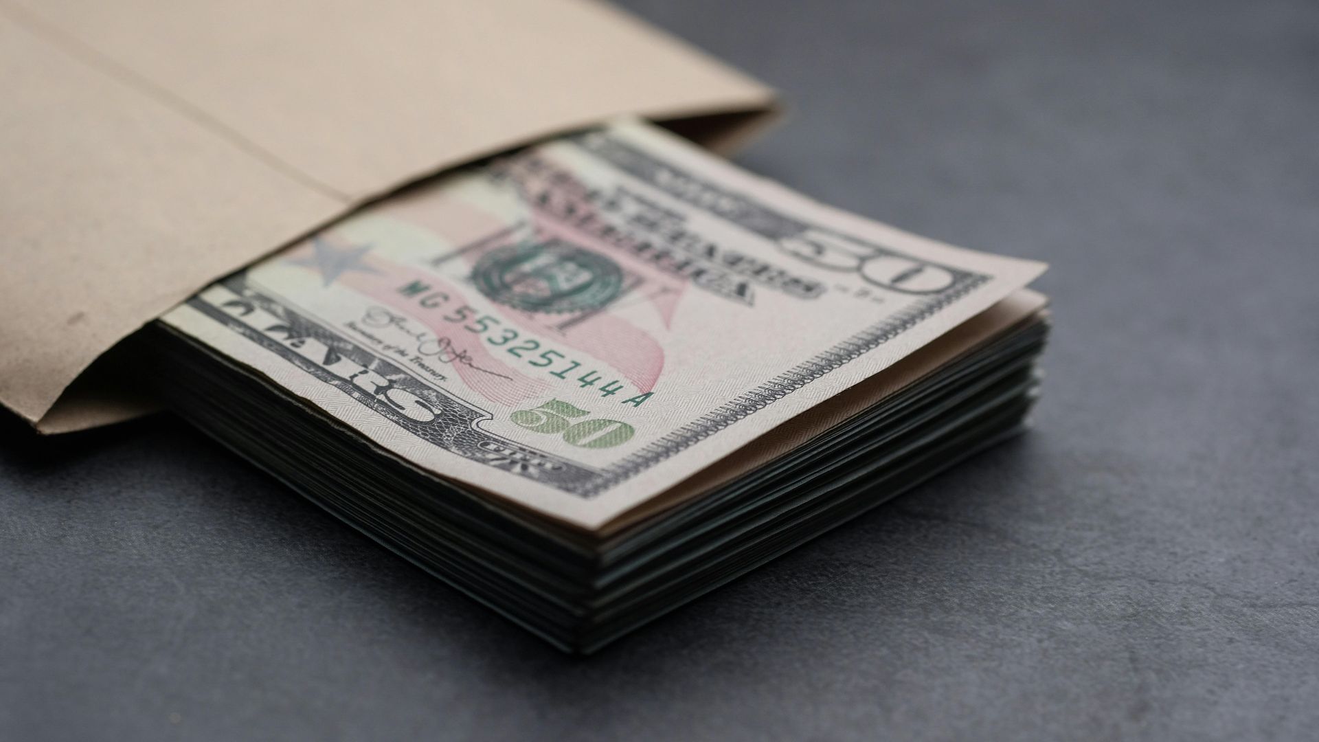 Close-up of US fifty dollar bills partially enclosed in a brown envelope, symbolizing finances.