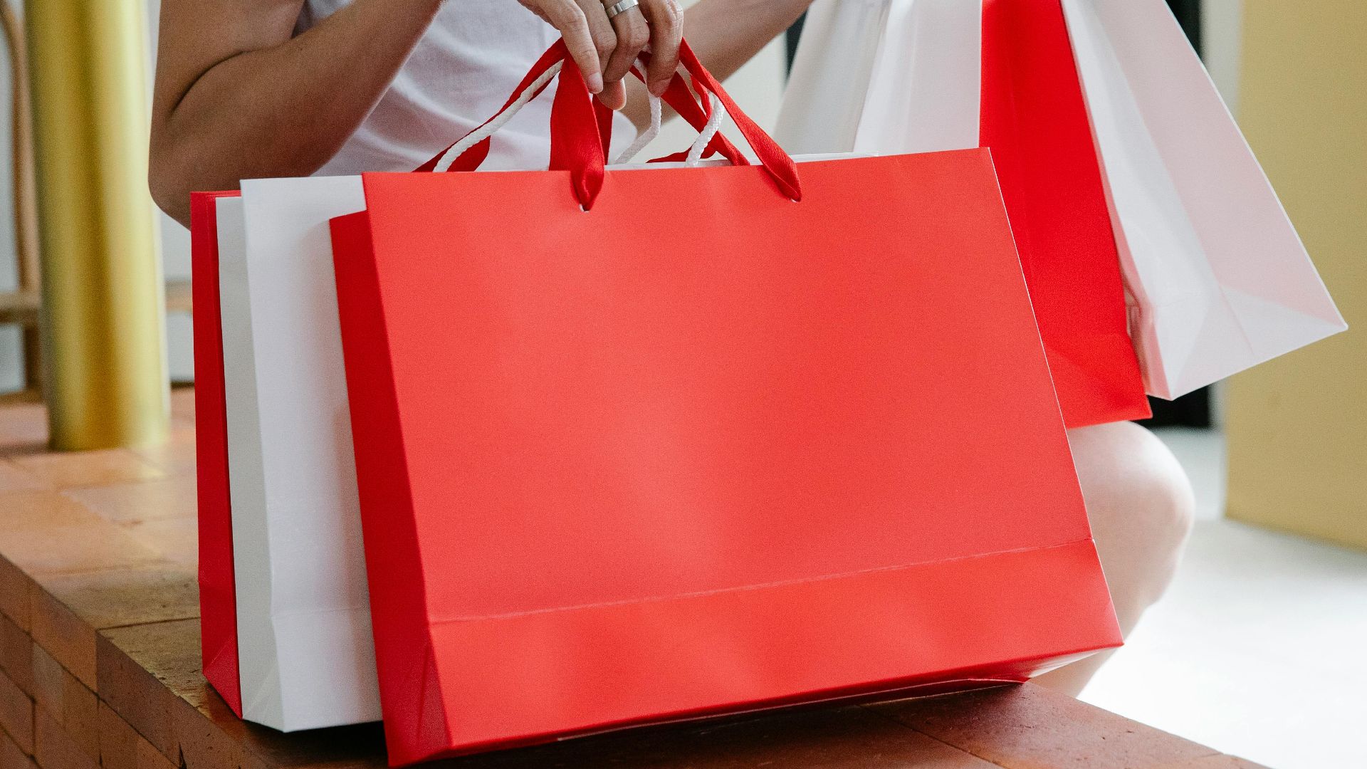 Side view of crop anonymous female buyer in white t shirt sitting on bench with many shopping bags in daylight