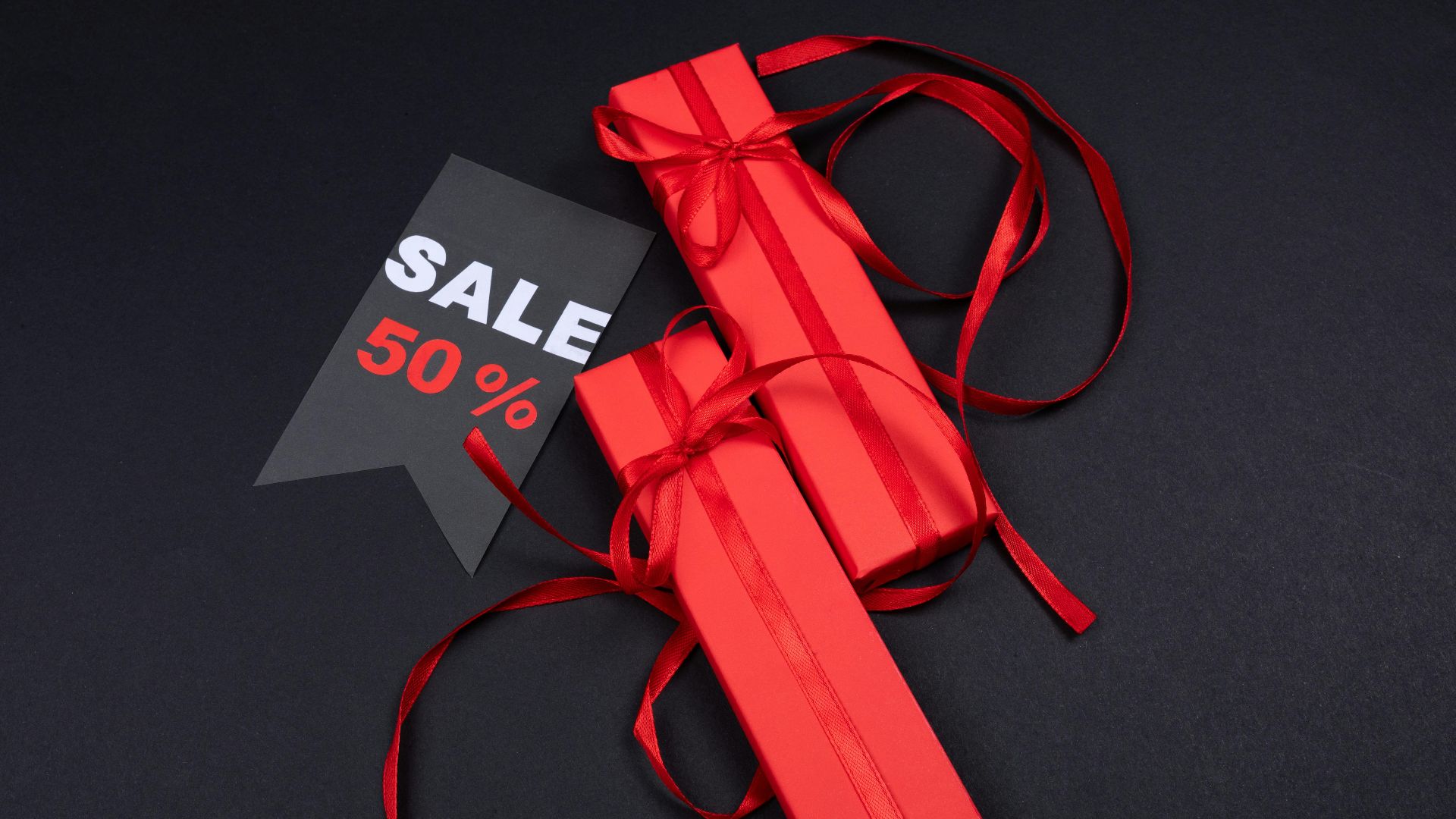Red gift boxes with ribbons and a 50% sale tag on a dark background.