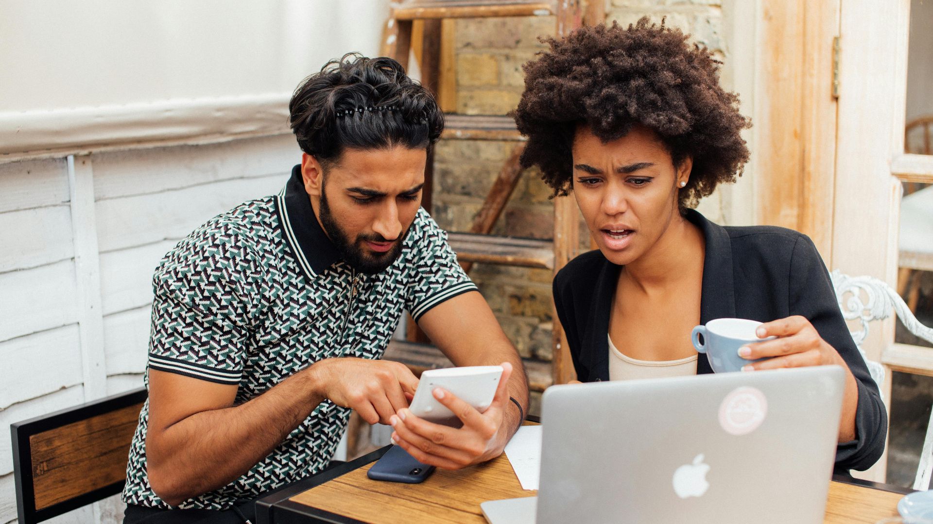 Two colleagues intensely working together with a laptop and phone, expressing surprise.