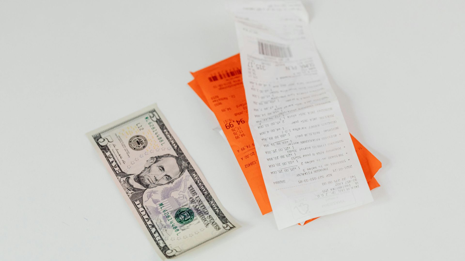 Close-up of a five-dollar bill next to shopping receipts on a white background, ideal for finance and retail themes.