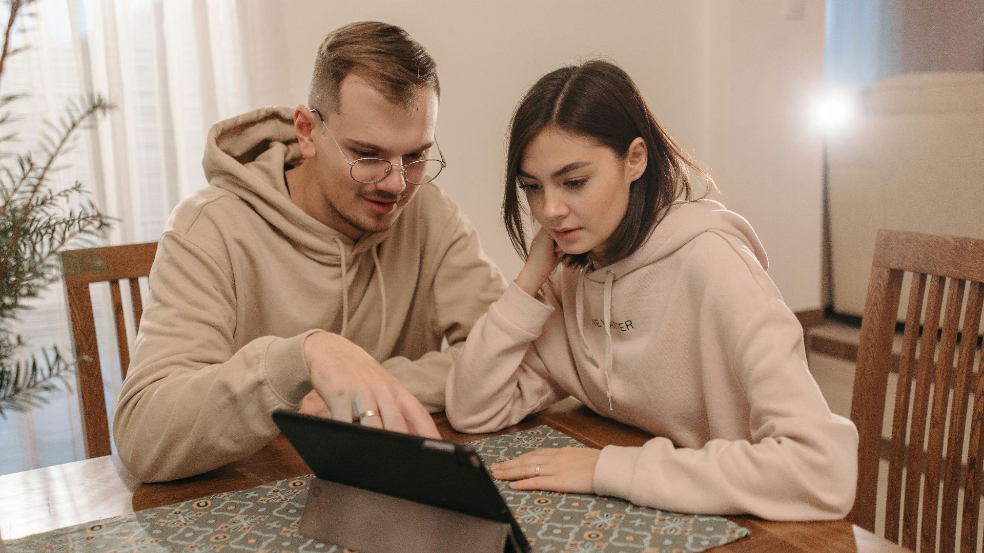 Young couple in hoodies browsing on a tablet together at home.