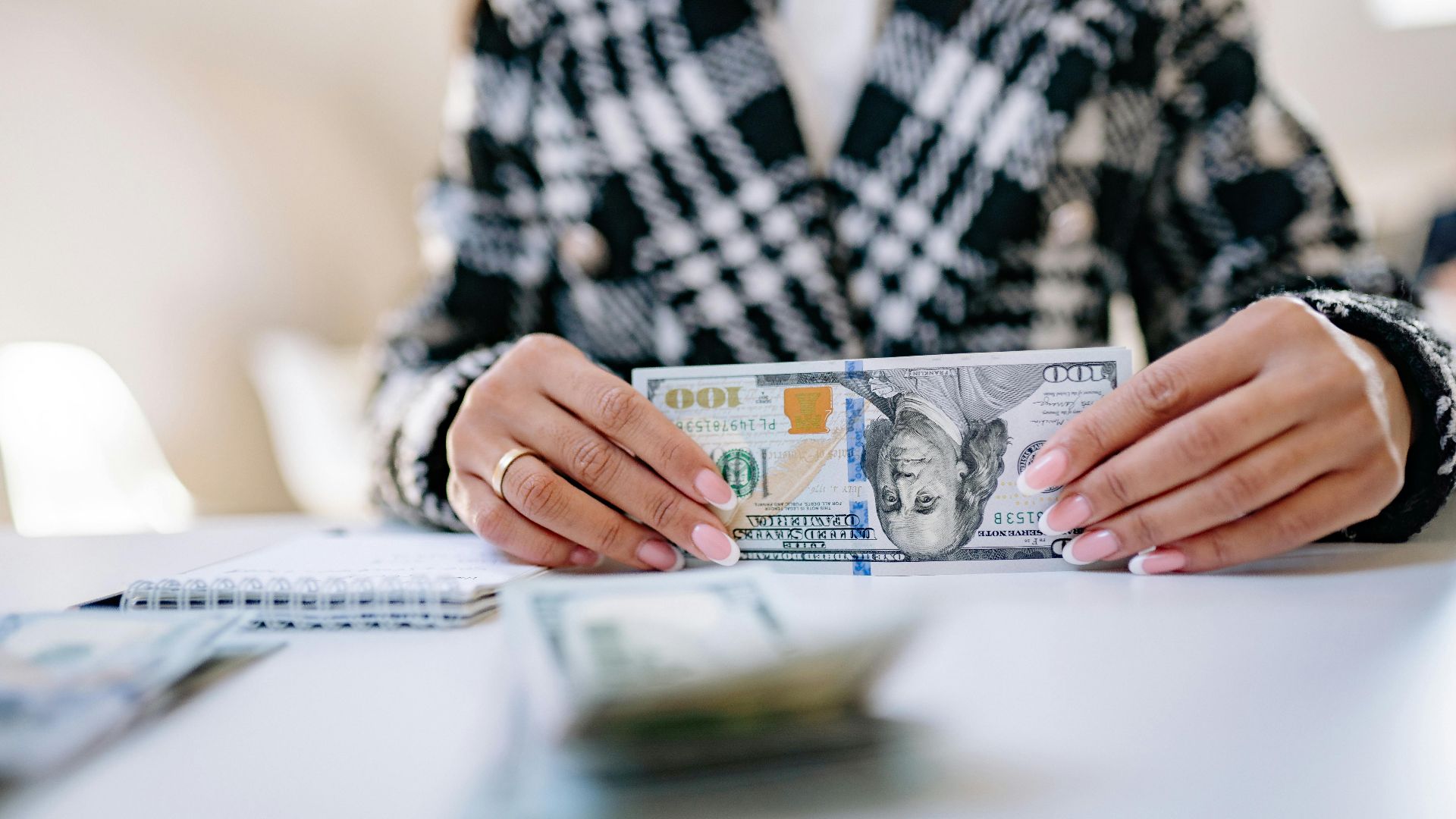 Close-up image of hands holding a US hundred dollar bill on a desk.