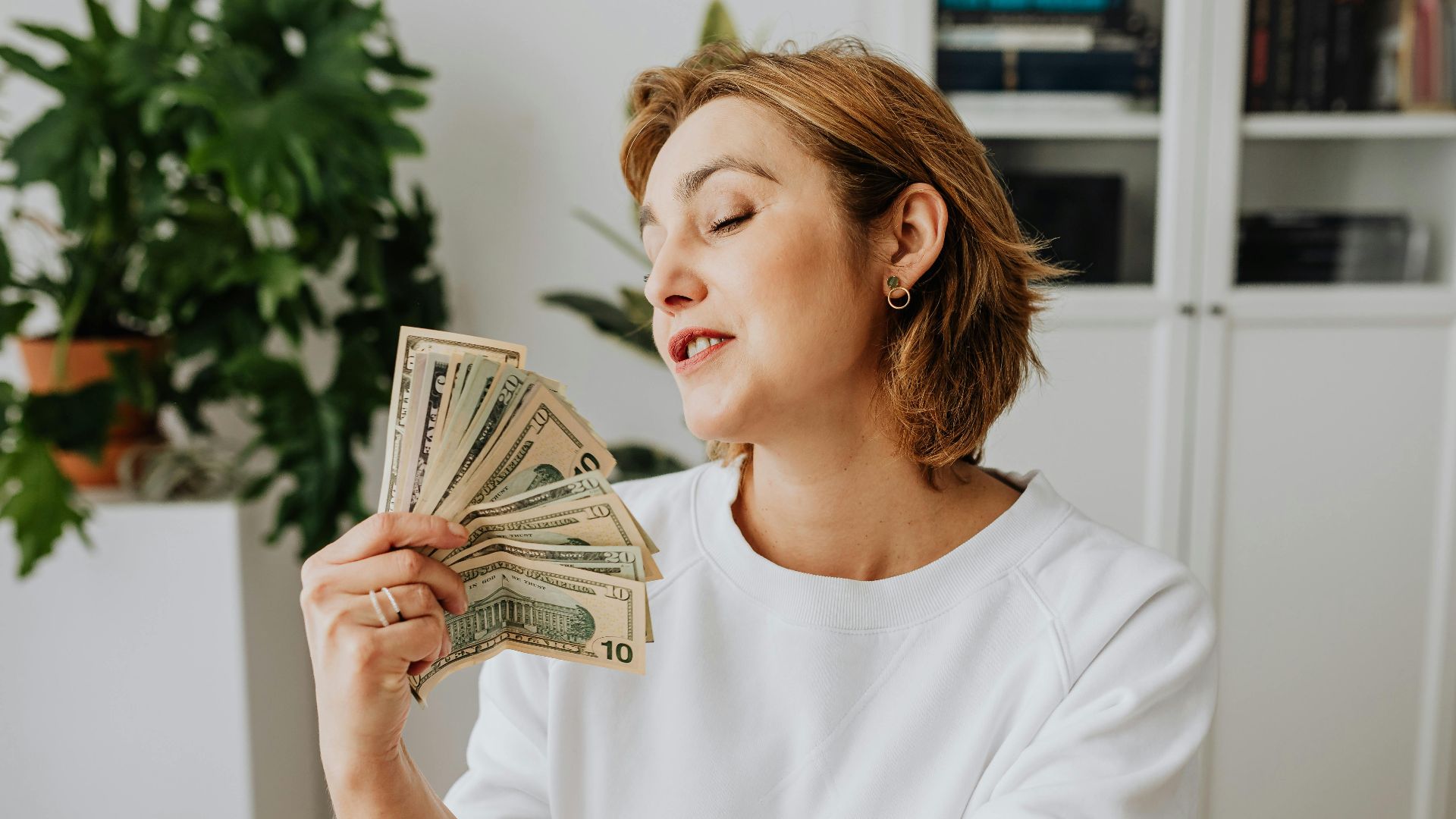 Woman holding US dollars in a relaxed indoor setting, reflecting satisfaction and success.