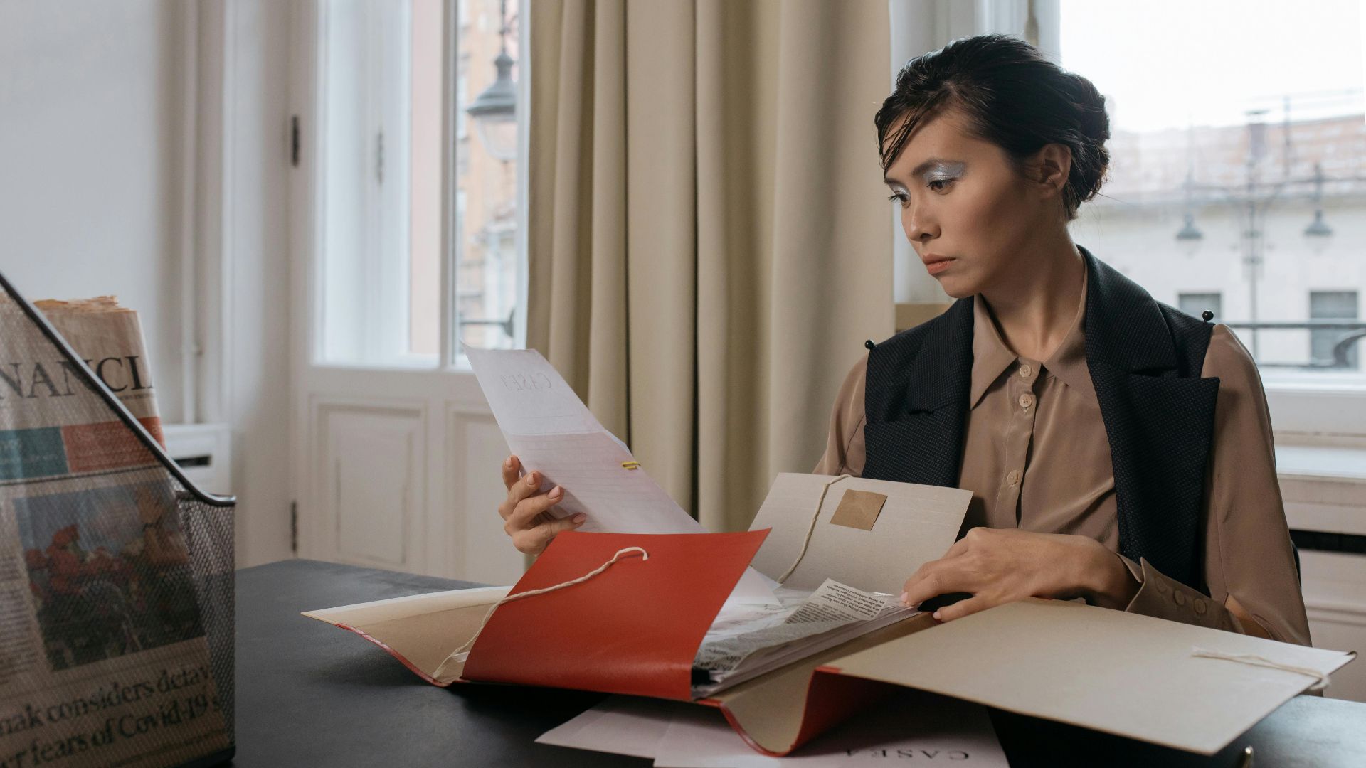 Businesswoman in an office setting reviewing important documents from a red folder with focus and determination.