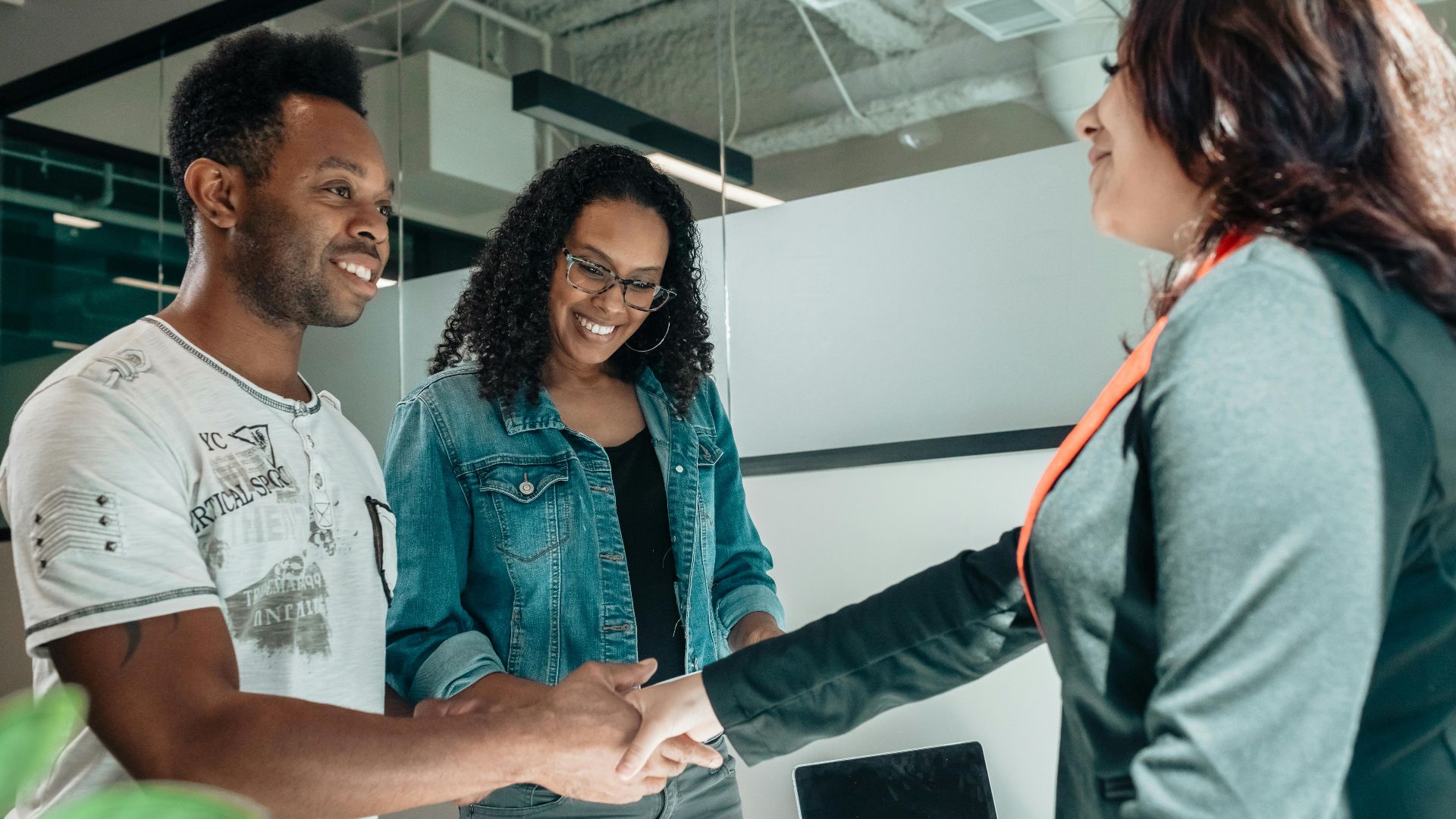 Smiling couple shaking hands with advisor in modern office.