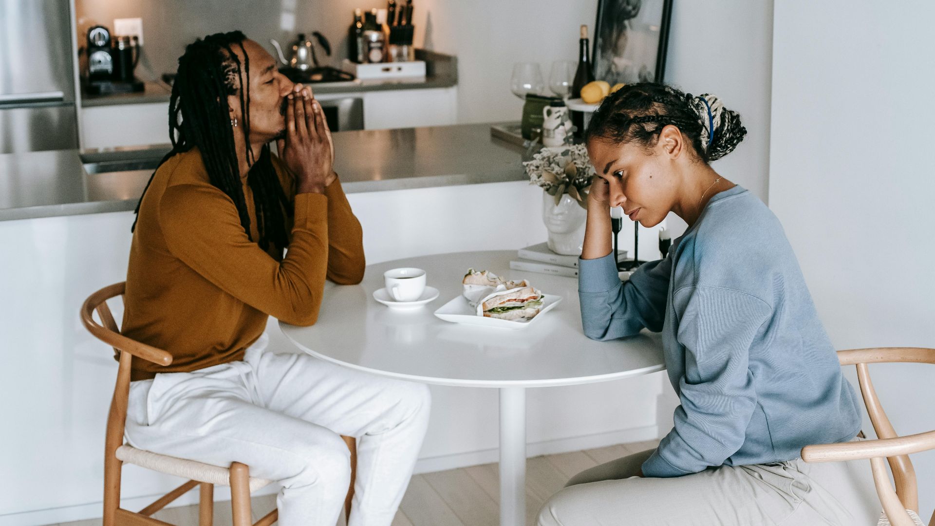 Young African American man sitting at table with woman and looking down thoughtfully while having conflict