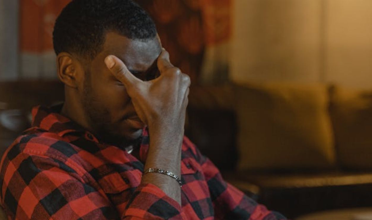 Man in Red Black and White Plaid Dress Shirt Sitting on Brown Wooden Armchair Feeling Exhausted