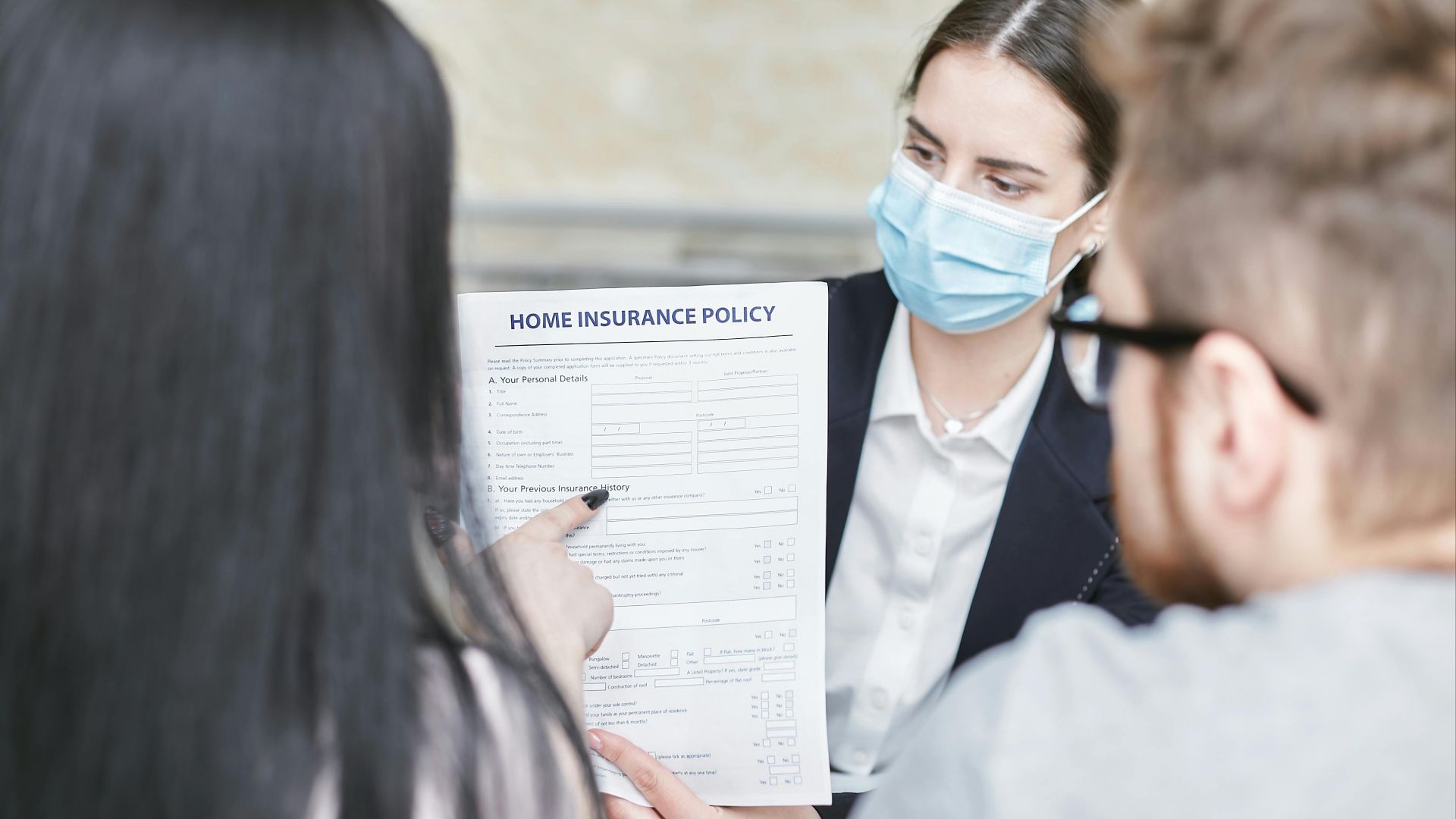 A professional woman explains a home insurance policy to clients during a meeting. Indoors setting.