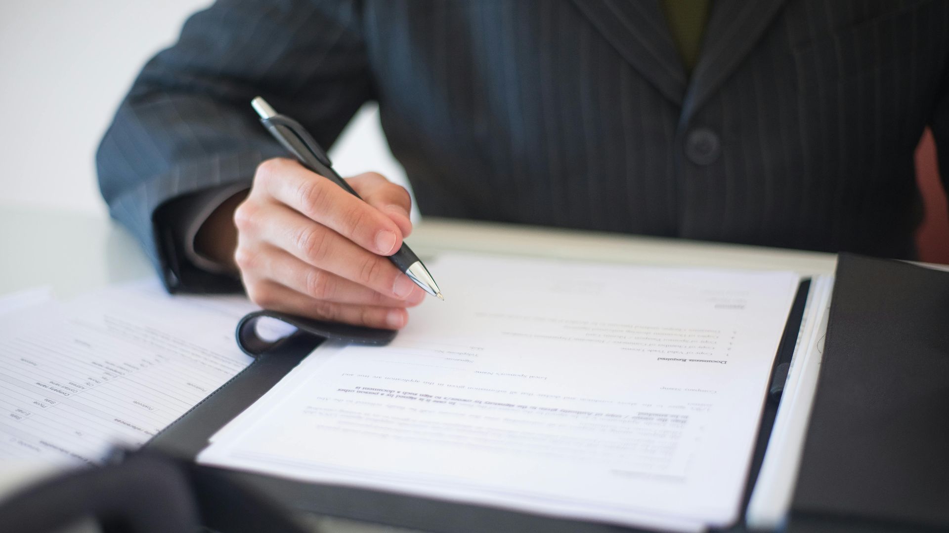 Close-up of a hand signing documents with a pen, symbolizing an important business contract.