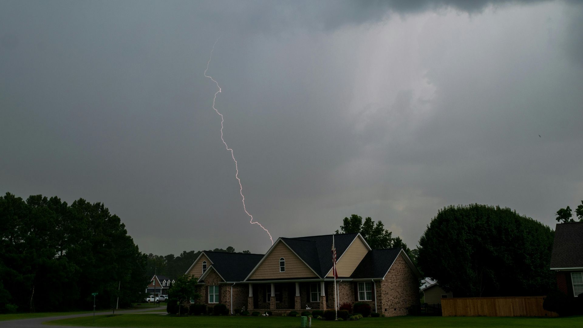 A vivid lightning bolt pierces the sky over suburban houses during a storm, capturing nature's raw power.