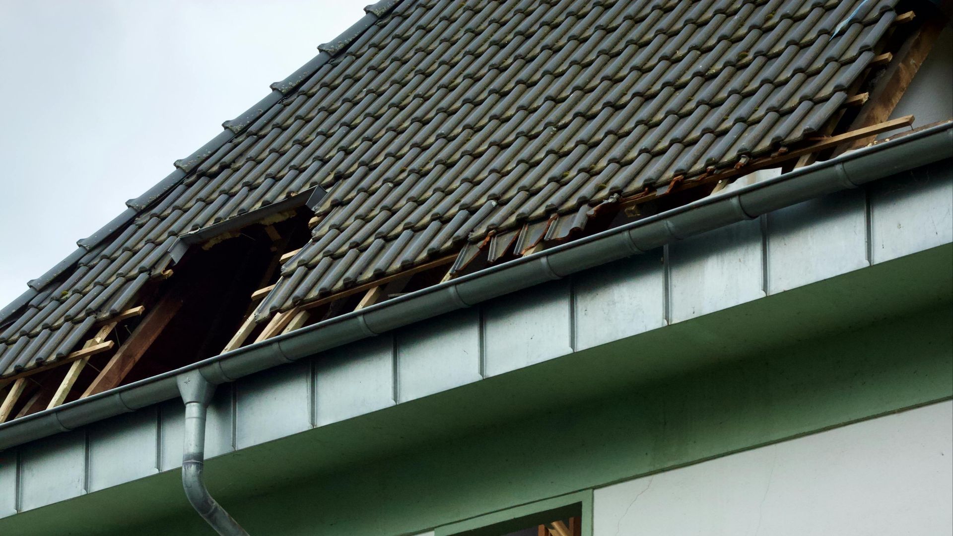 An exterior view of a damaged house showing a broken roof and exposed interior structure.