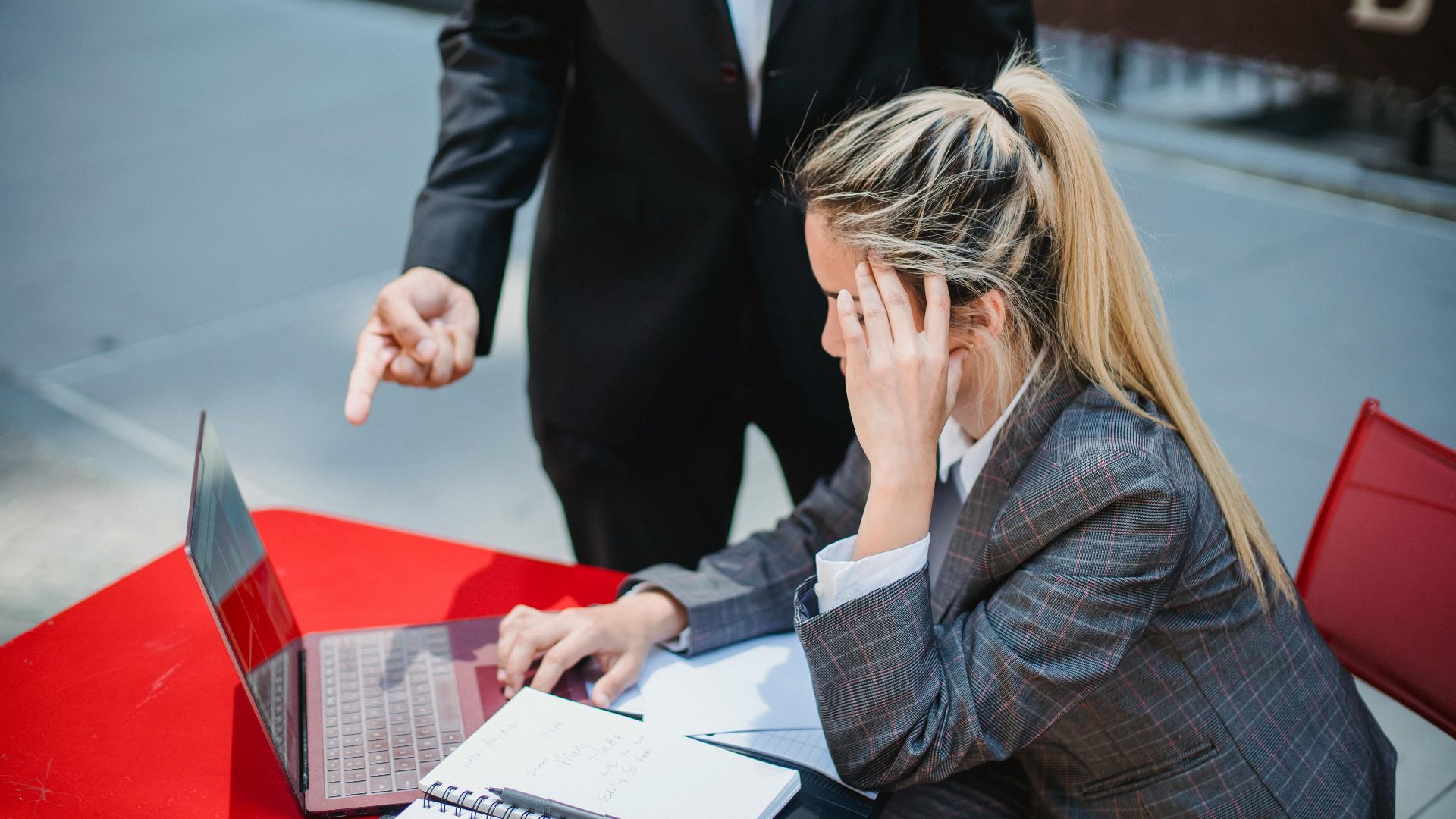 Business professionals discussing work on a laptop at an outdoor red table.