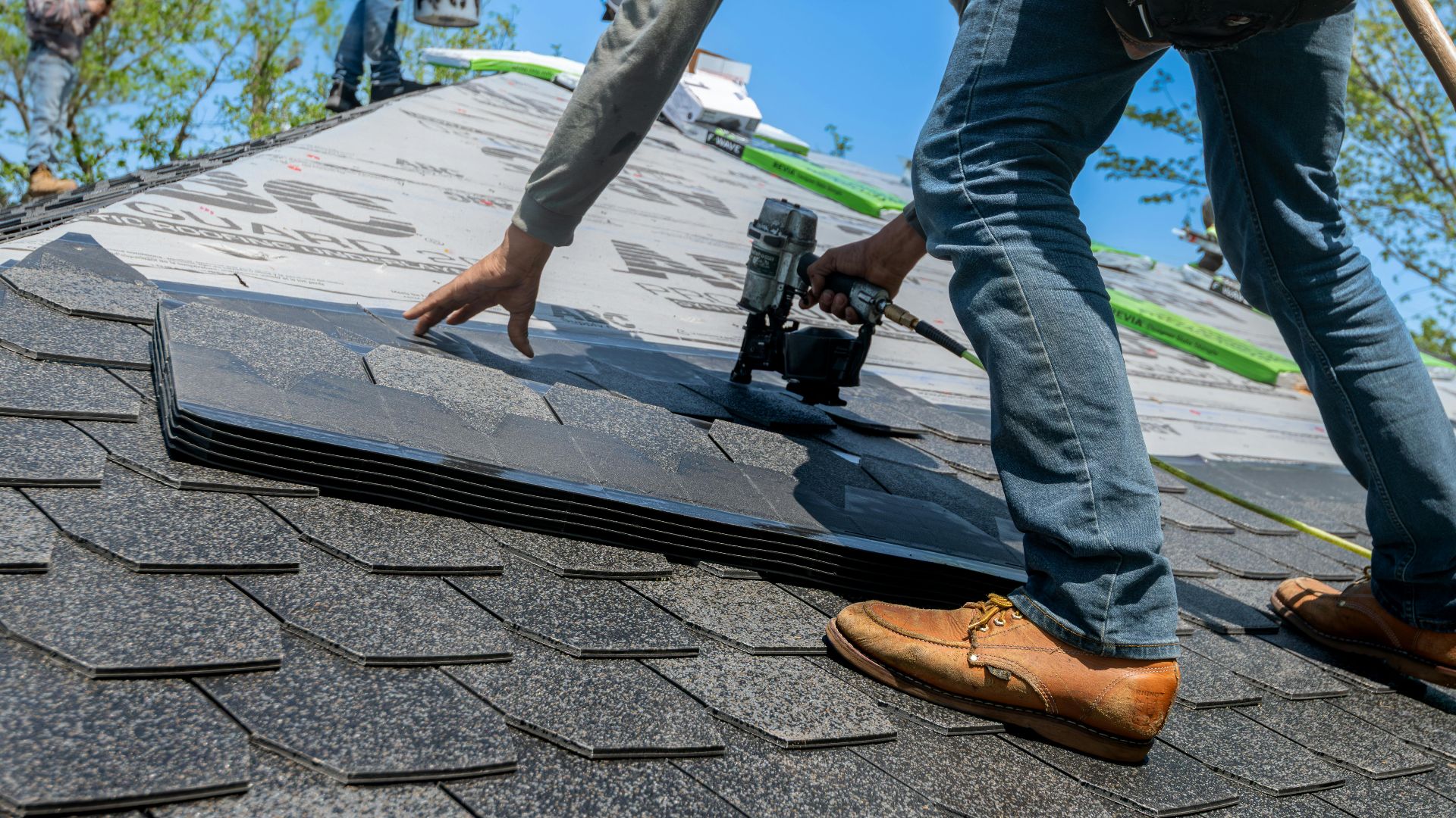 Roofer using nail gun for shingle installation on residential roof.
