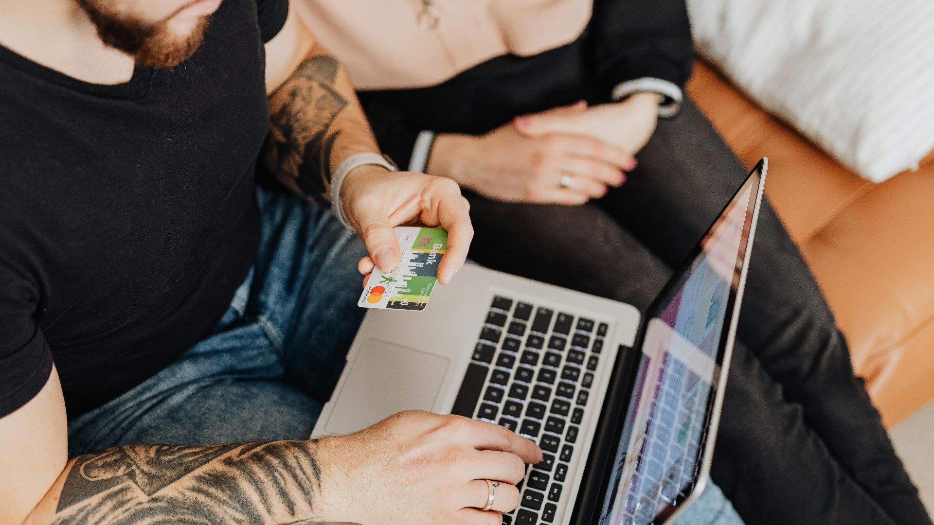 A couple casually shopping online using a laptop and credit card in a cozy indoor setting.