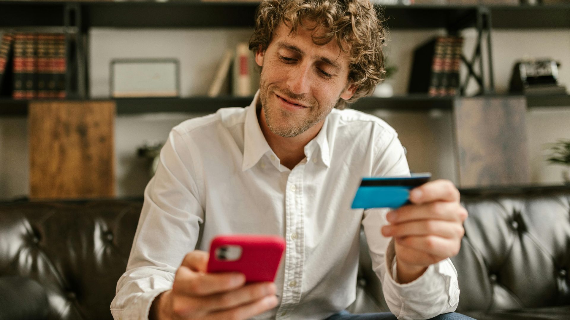Caucasian man using smartphone and credit card for online shopping indoors.